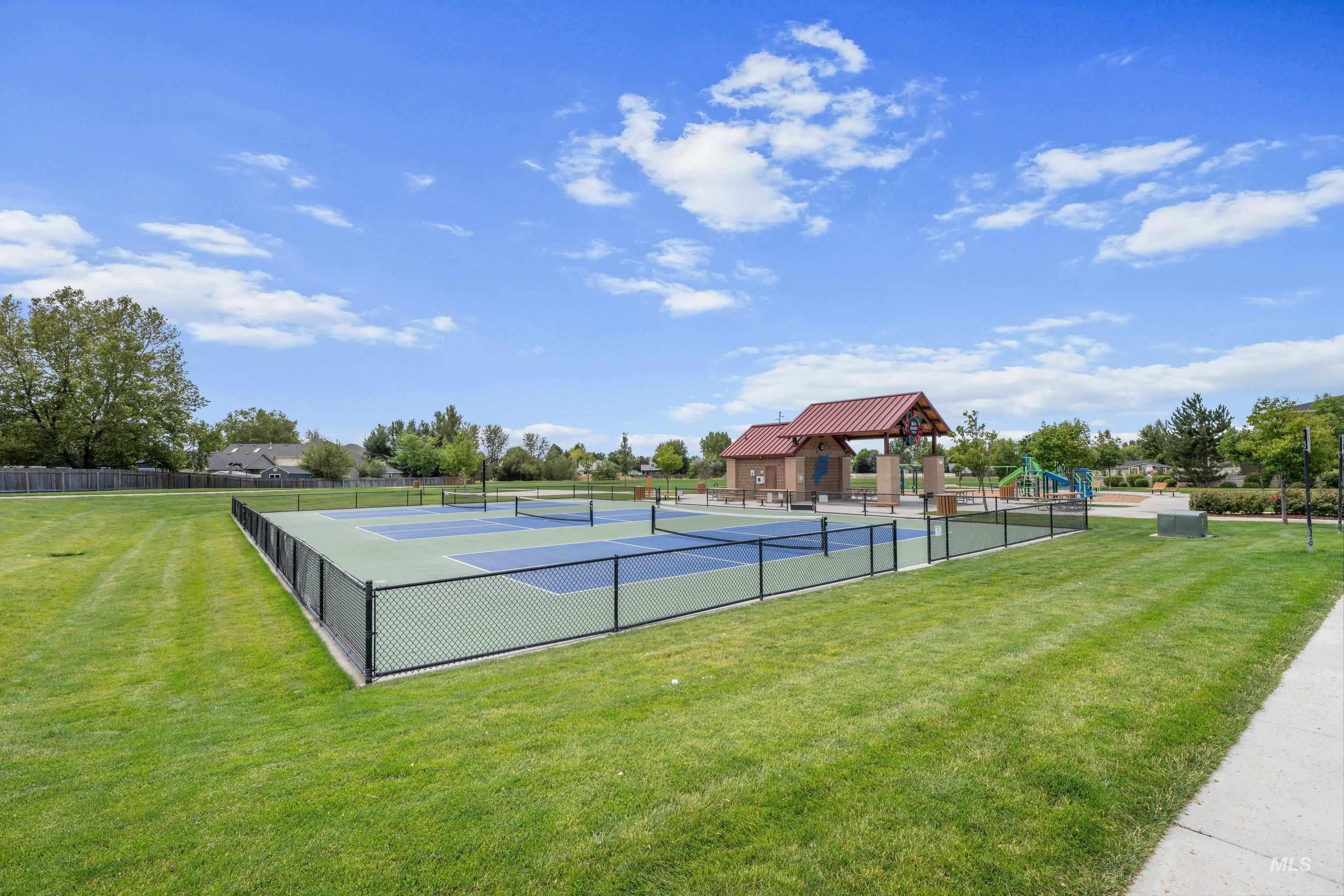 Fenced recreational courts featuring a multi-sport surface, surrounded by expansive green space