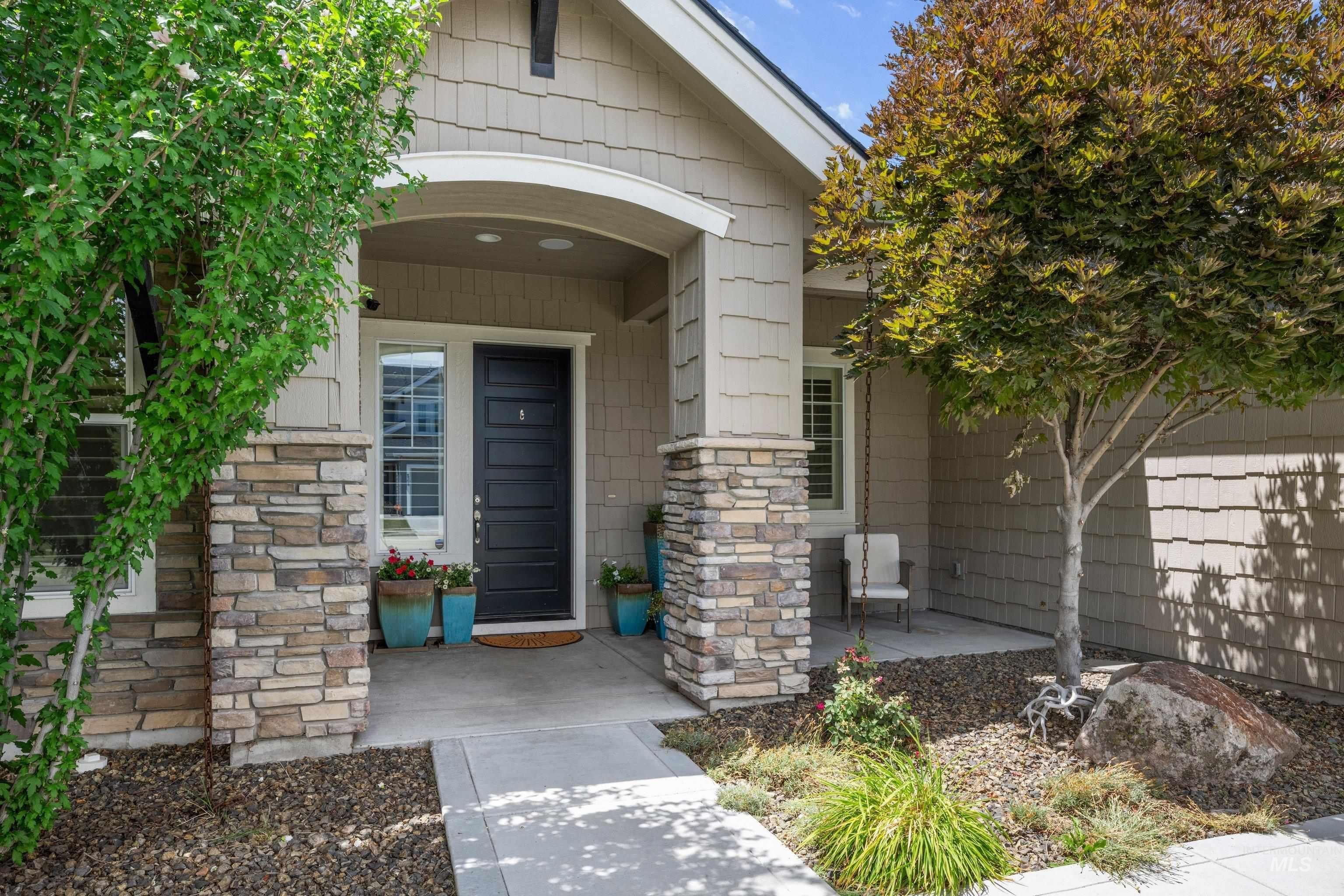 Inviting entry featuring a covered porch, stacked stone pillars, shake siding, a paneled front door, and a concrete walkway