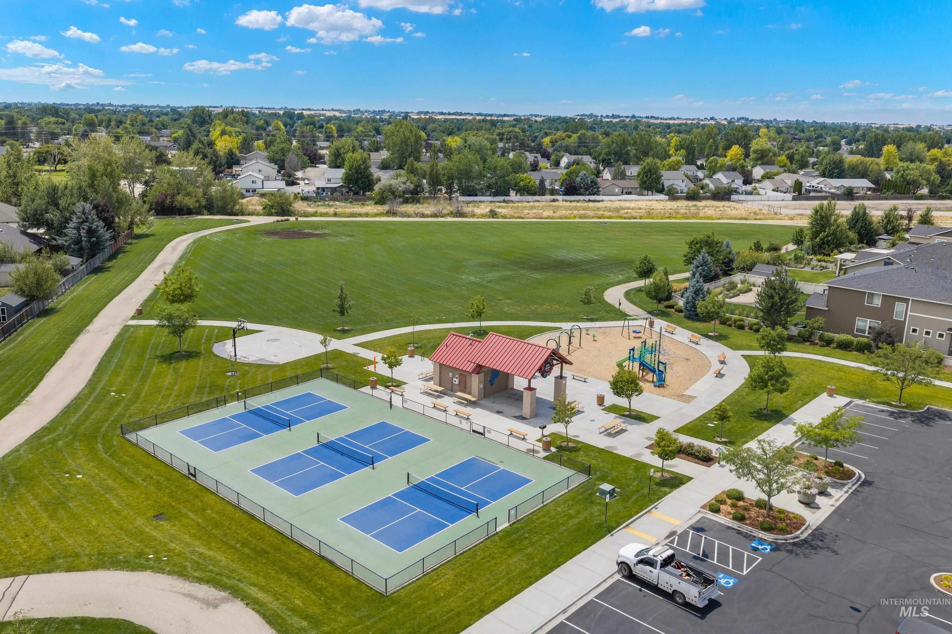 Community recreational area featuring multiple pickleball courts, a playground with sandbox, a covered picnic shelter, and paved walking paths