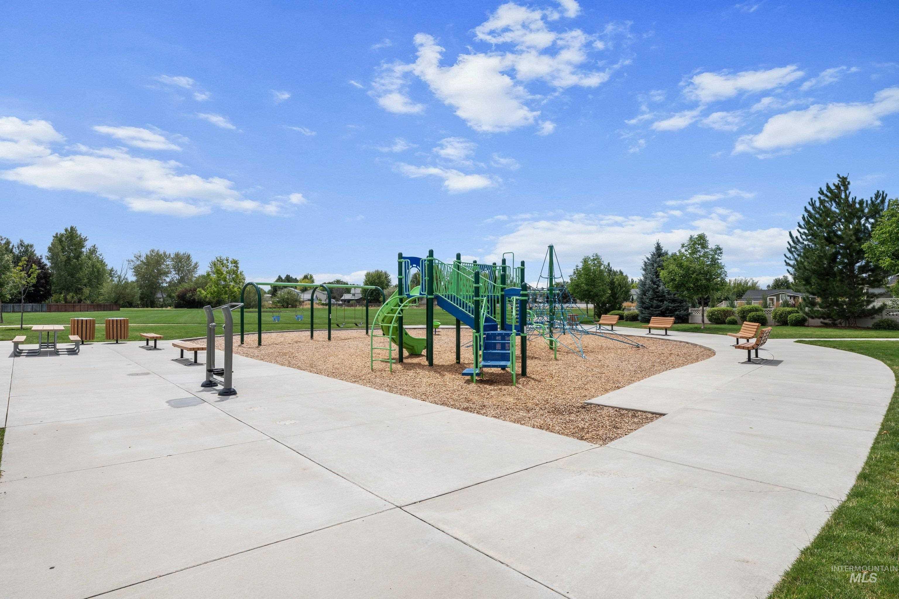 Community park featuring a playground with slides and swings, a picnic area with a table and benches, outdoor fitness equipment, and a paved walking path