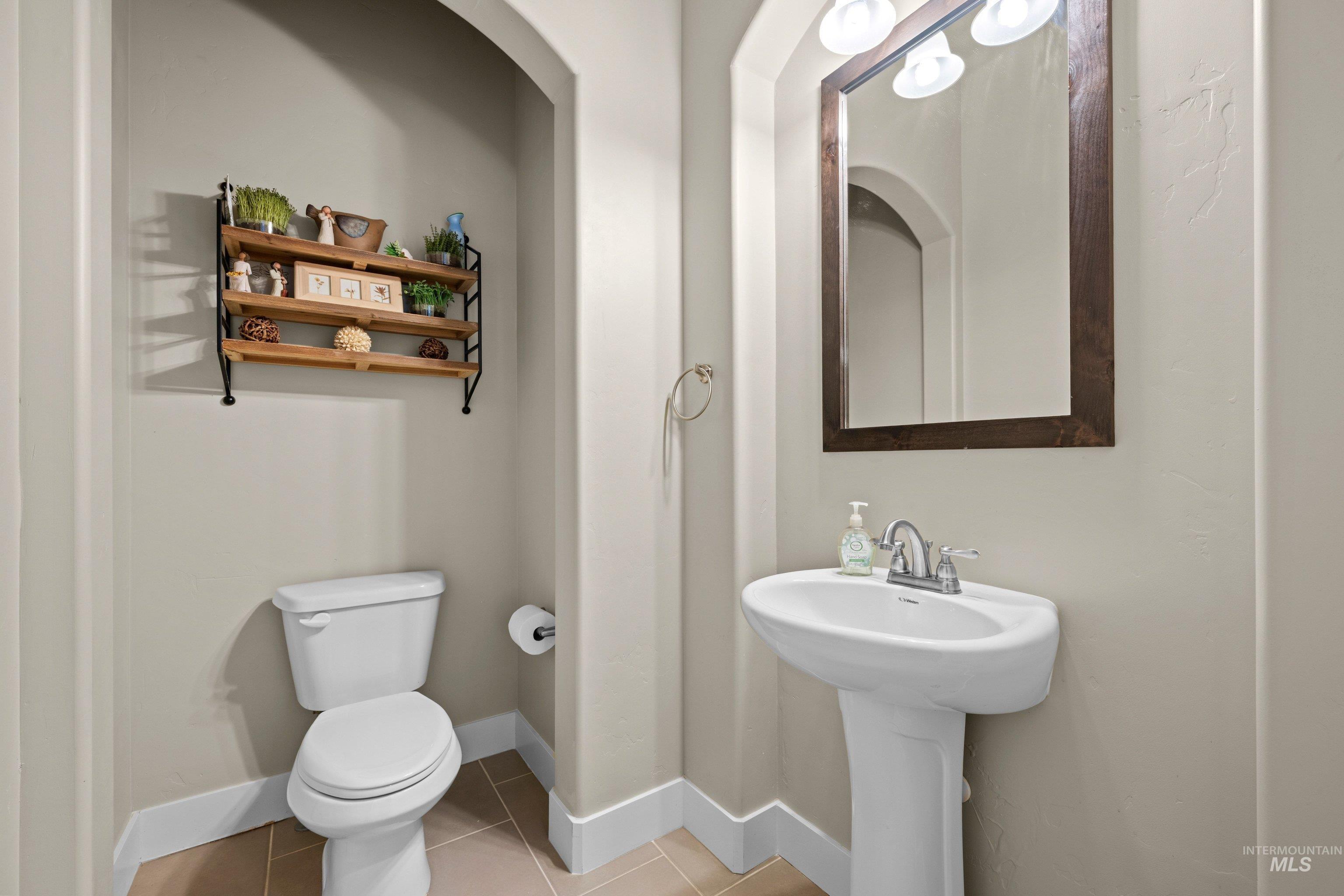 Powder room featuring a pedestal sink with chrome faucet, a rectangular mirror with a dark wood frame, and a three-tiered wood shelf with black metal supports