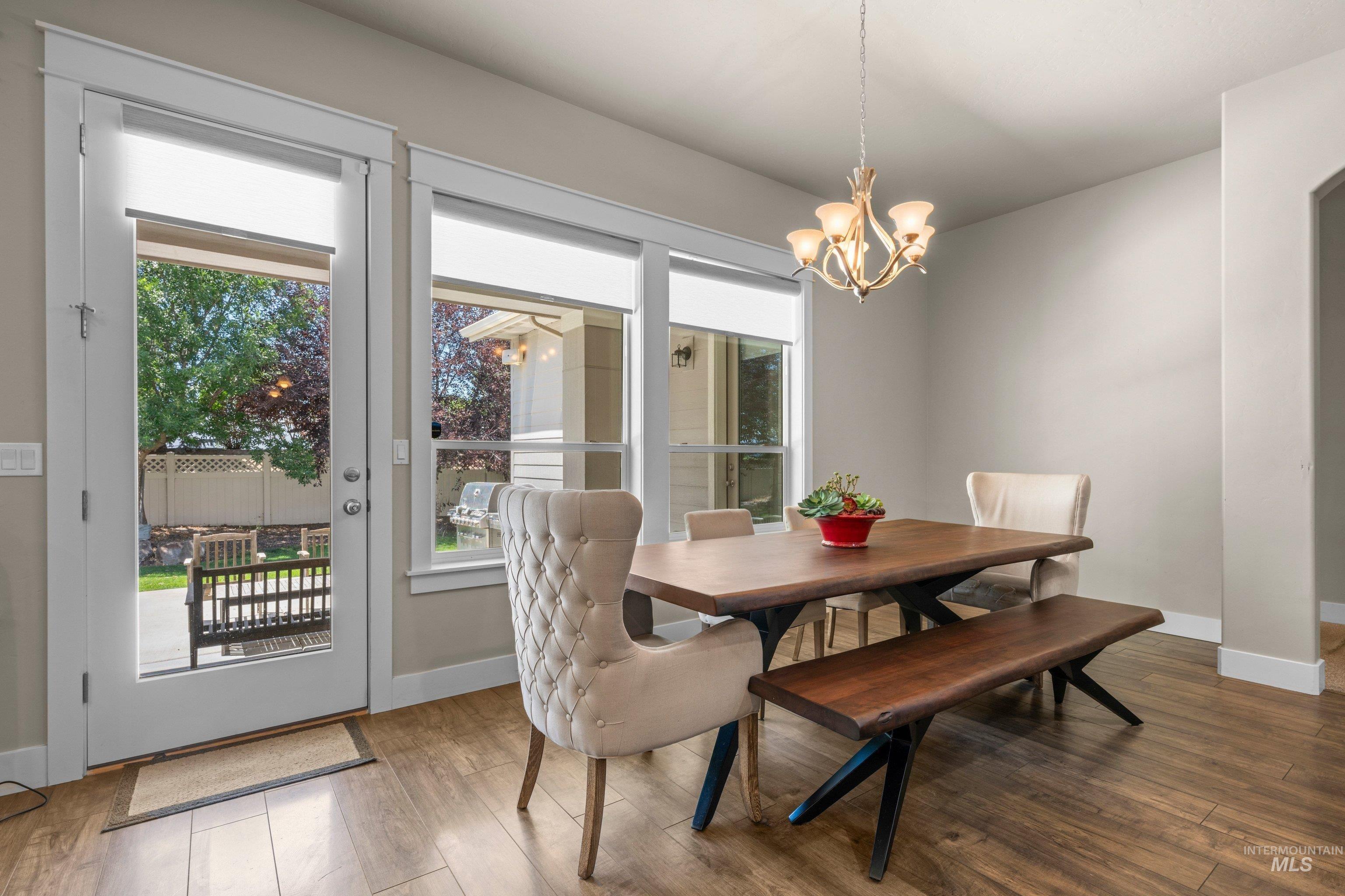 Dining area featuring wood-finish flooring, a contemporary chandelier, and a glass-paned door opening to an outdoor patio with a bench