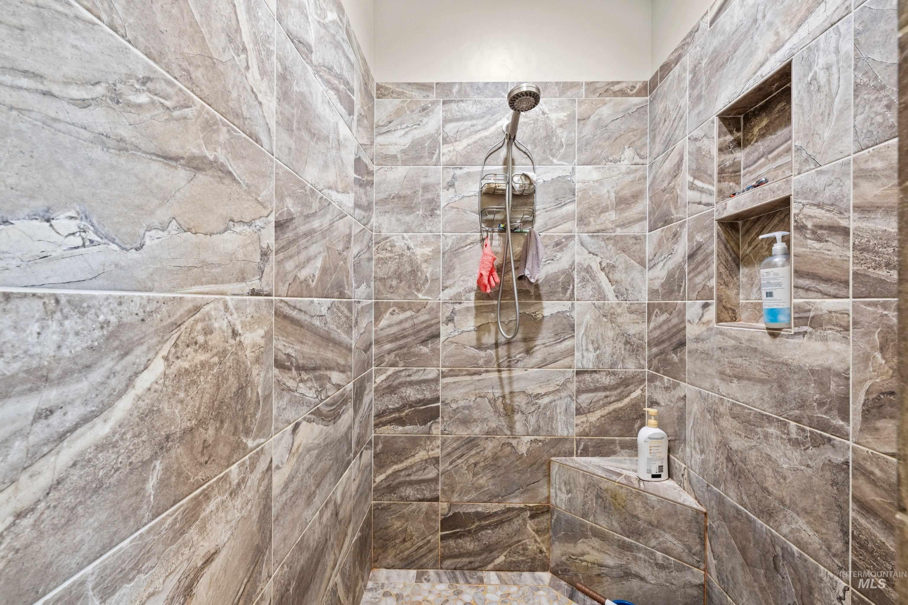Walk-in shower featuring large format natural stone-look tile, built-in corner bench, and recessed wall niches