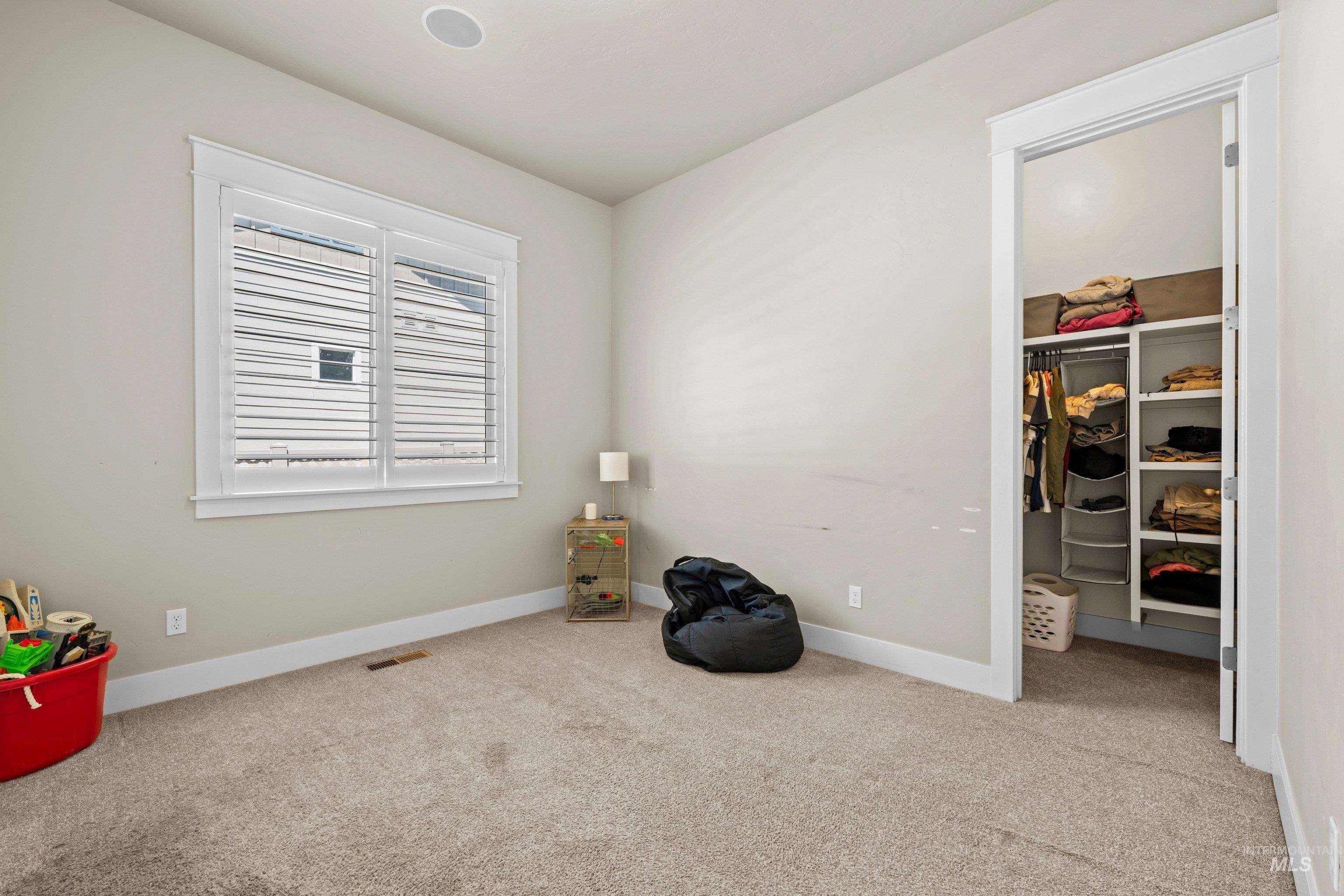 Carpeted room with a double-paned window featuring white plantation shutters, a recessed ceiling light, and an open closet with built-in shelving and hanging rods