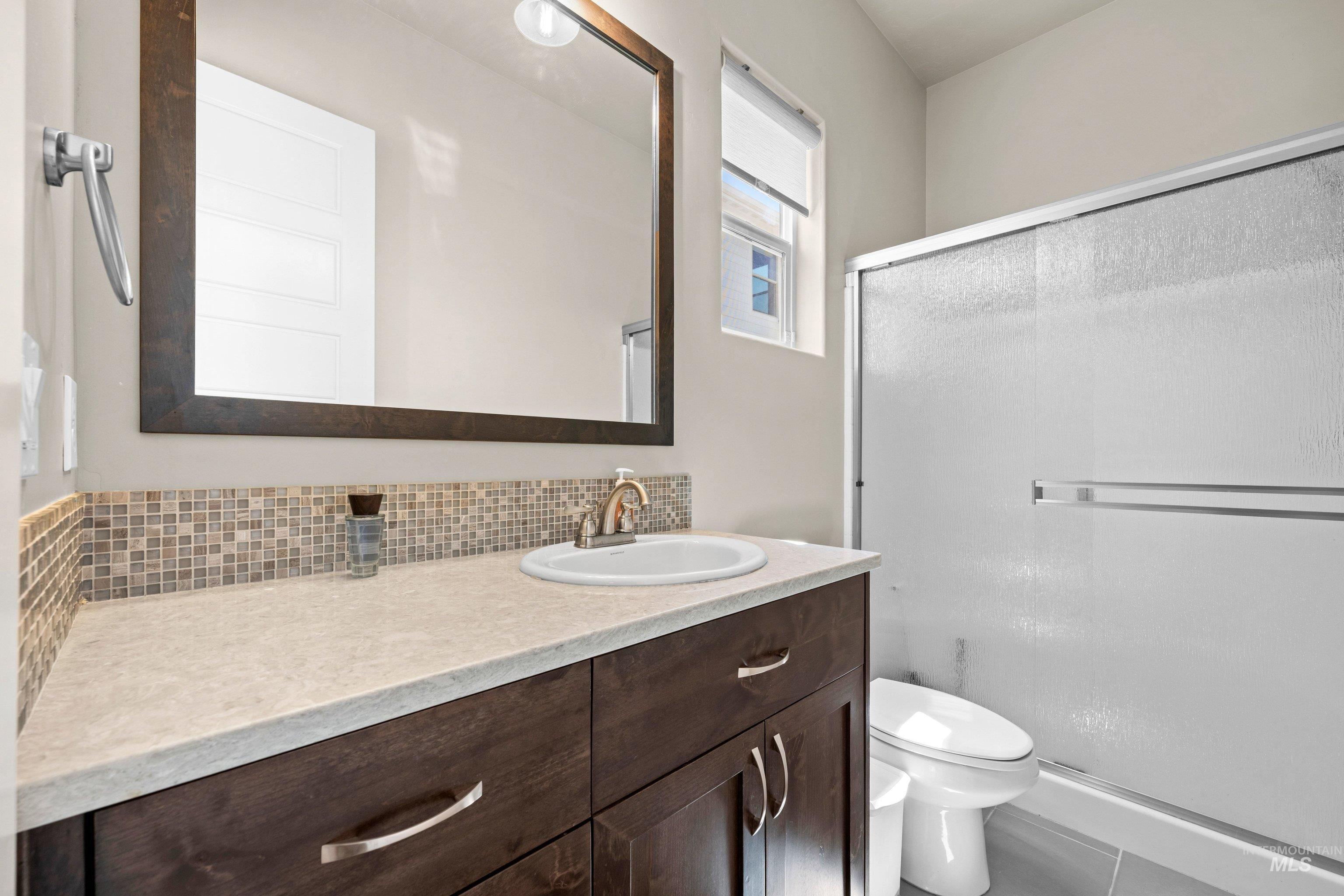 Bathroom featuring a dark wood-finish vanity with a light countertop, an integrated sink, and a mosaic tile backsplash