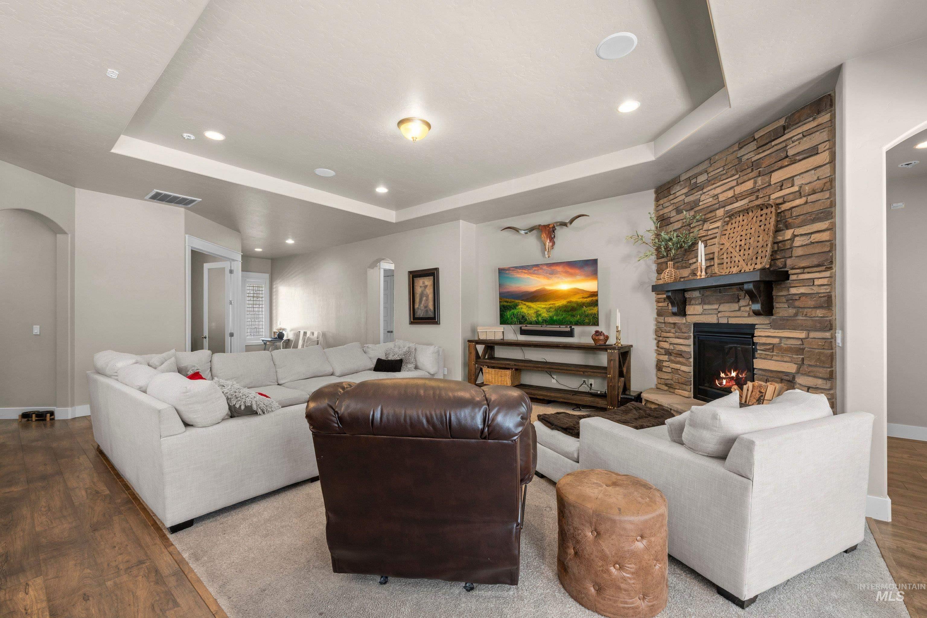 Living area featuring a stone accent wall, fireplace with mantel, tray ceiling, recessed lighting, and wood-finish flooring