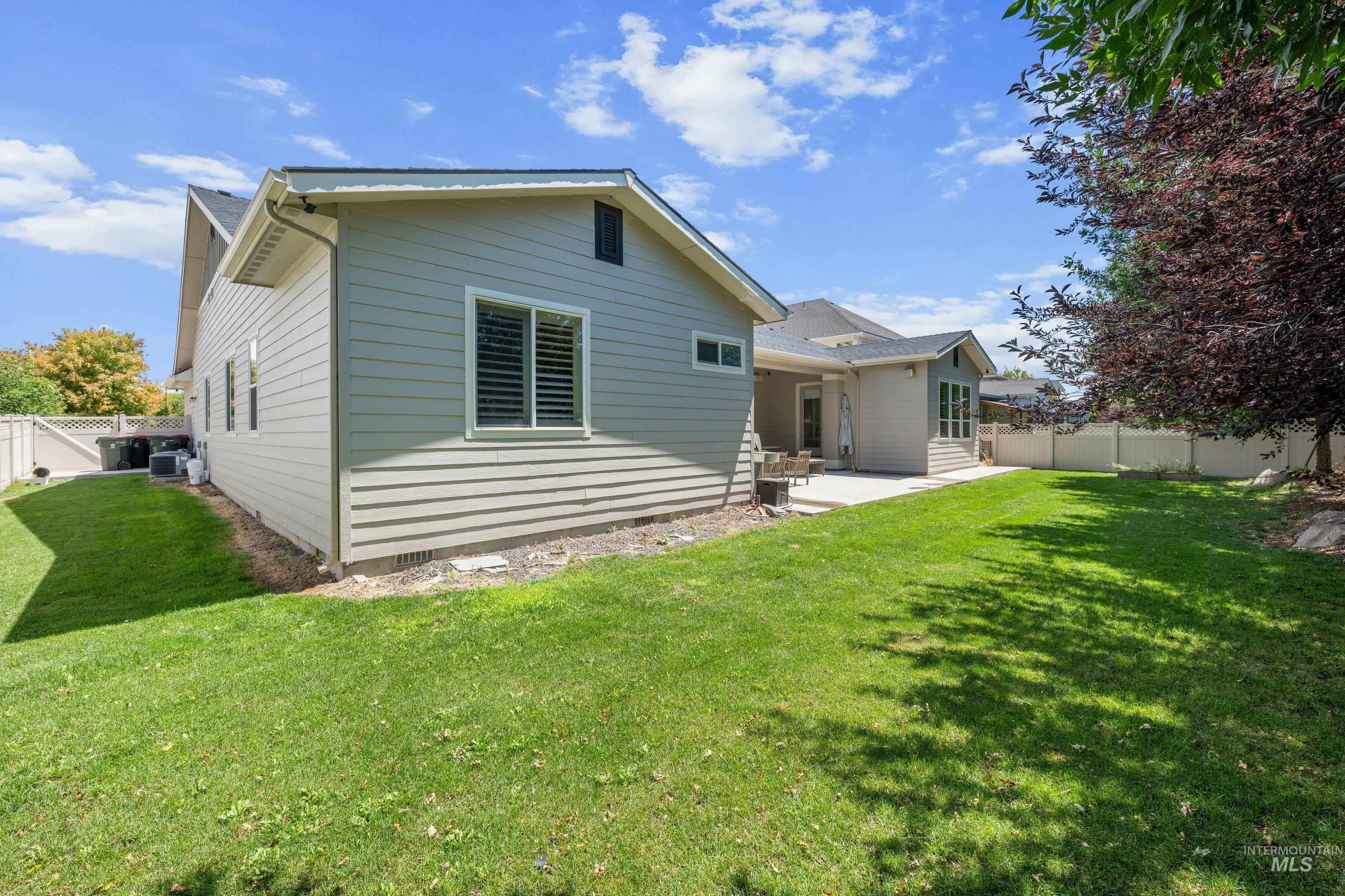 Spacious backyard featuring a manicured lawn, an expansive concrete patio, and mature trees