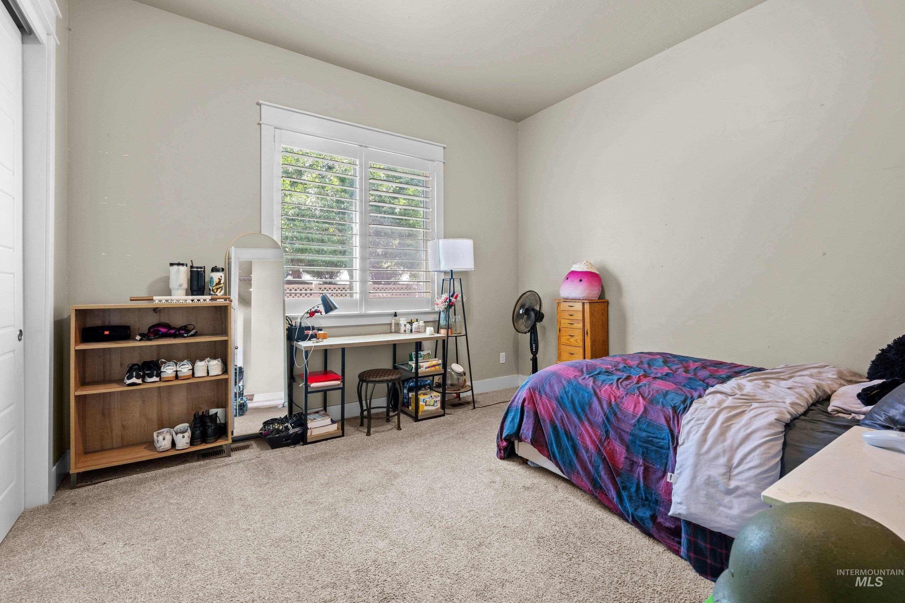 Bright room featuring neutral-toned walls, plush carpeting, and a window with white plantation shutters