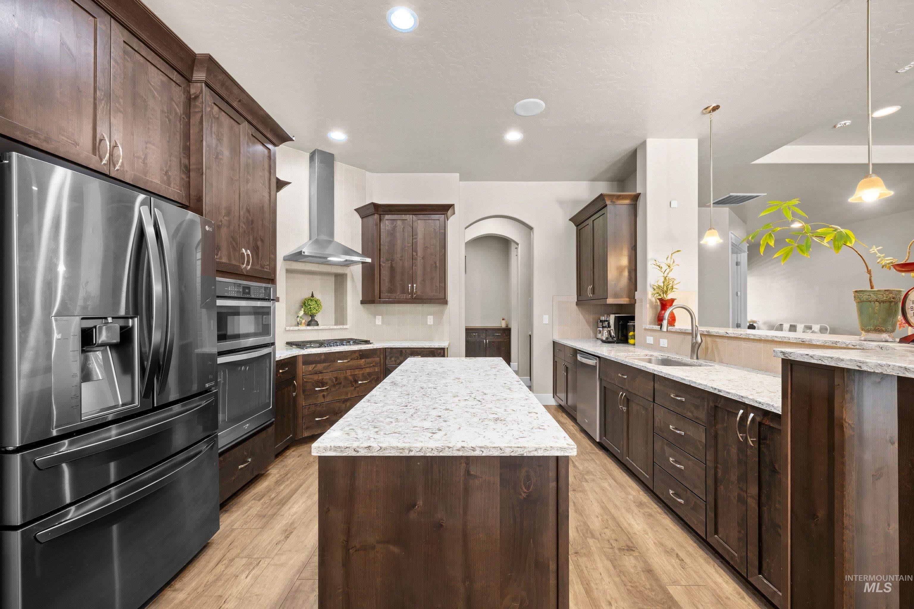 Kitchen featuring a central island with a light-toned countertop, wood-finish flooring, dark wood cabinetry, stainless steel appliances, and recessed lighting