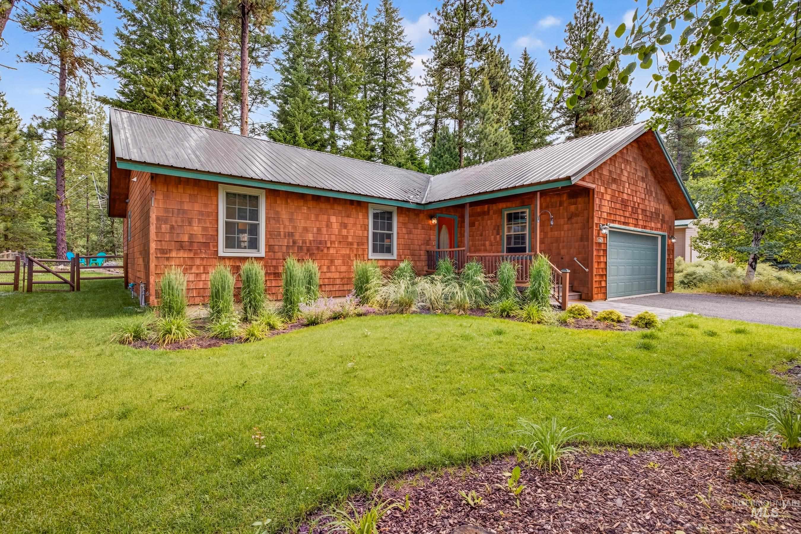 Cedar-shingled exterior featuring a covered porch entry, a metal roof, an attached garage with a green door, and surrounding mature trees
