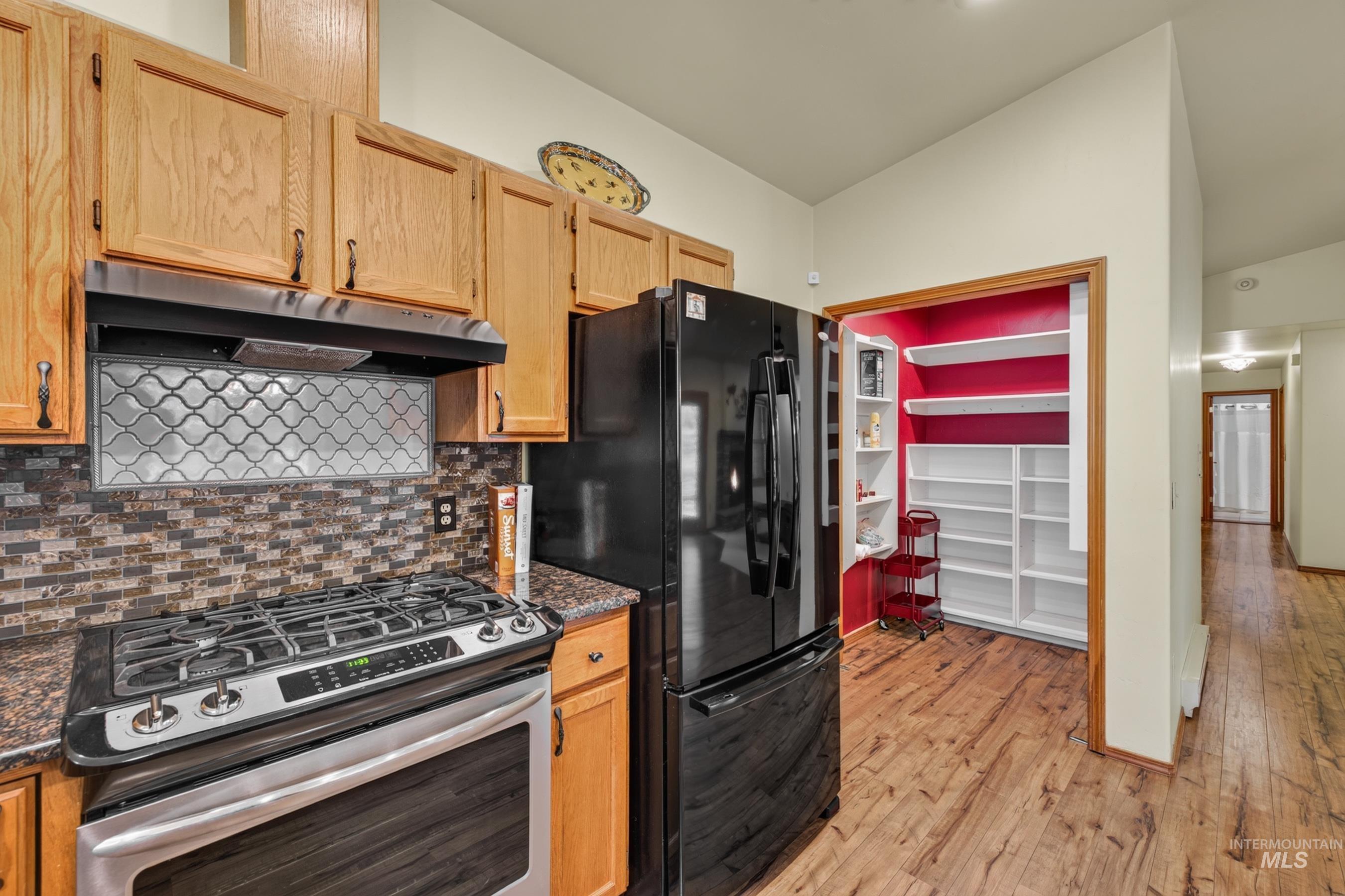 Kitchen featuring wood-finish flooring, oak cabinetry with dark hardware, granite-look countertops, and a tiled backsplash