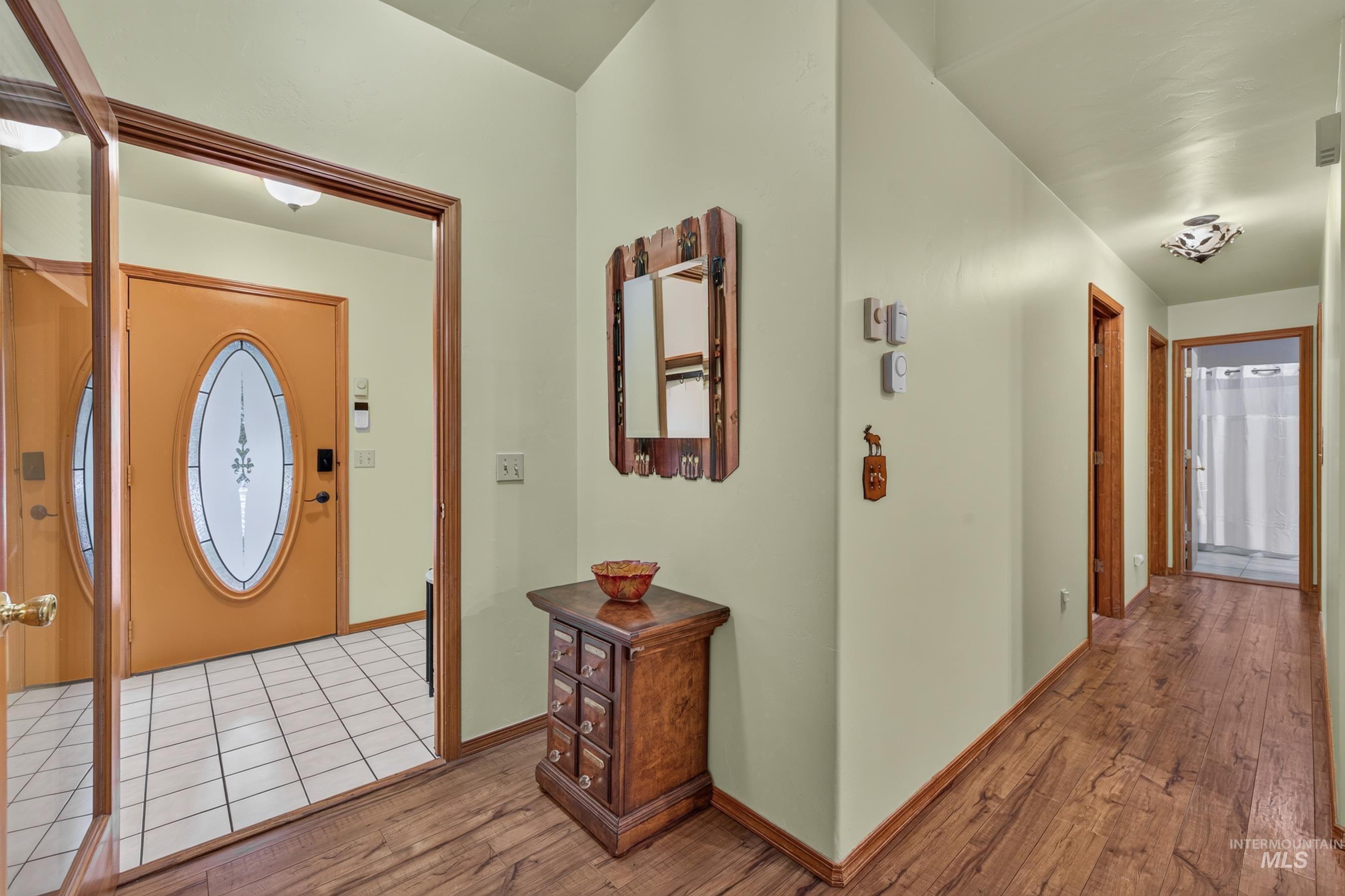 Entryway featuring a decorative front door with an oval glass insert, wood-finish flooring, a tiled floor entry area, and a hallway with additional wood-paneled doorways