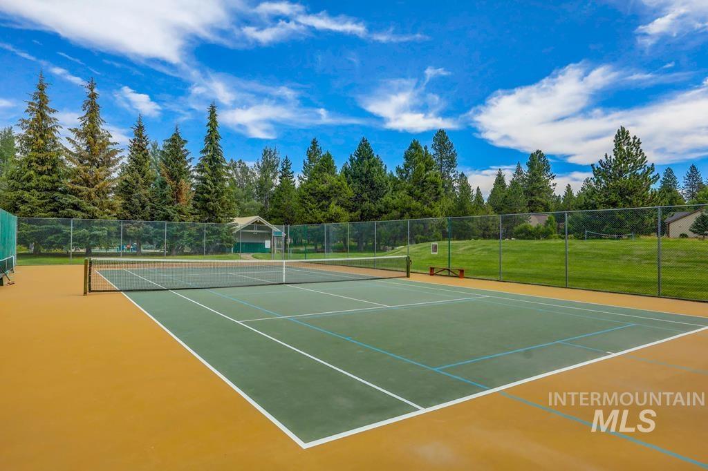 Recreational tennis court with green and gold playing surfaces, full perimeter fencing, and mature tree-lined surroundings