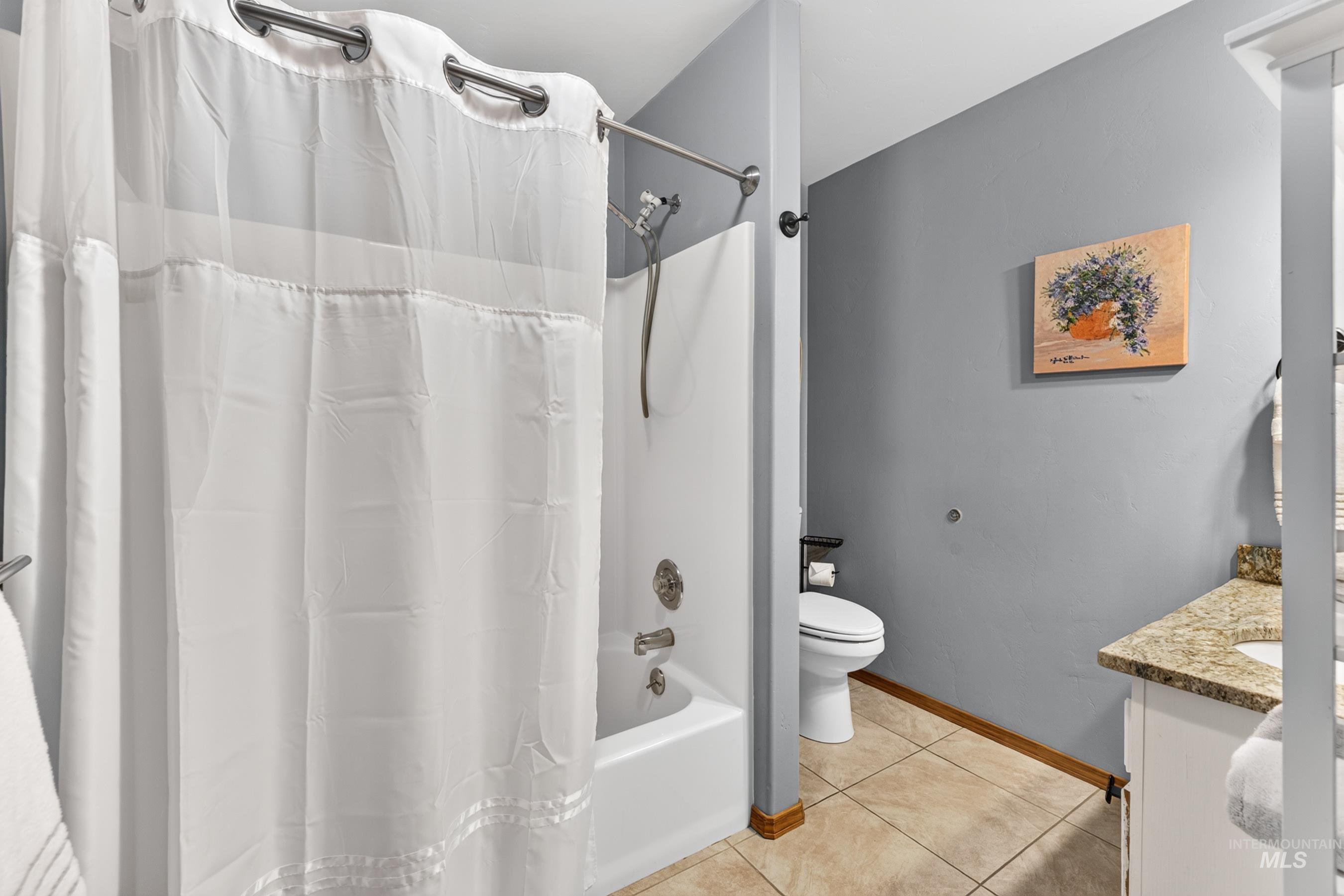 Bathroom featuring a shower-tub combination with white surround, a toilet, a vanity with a light-toned countertop, and tile flooring
