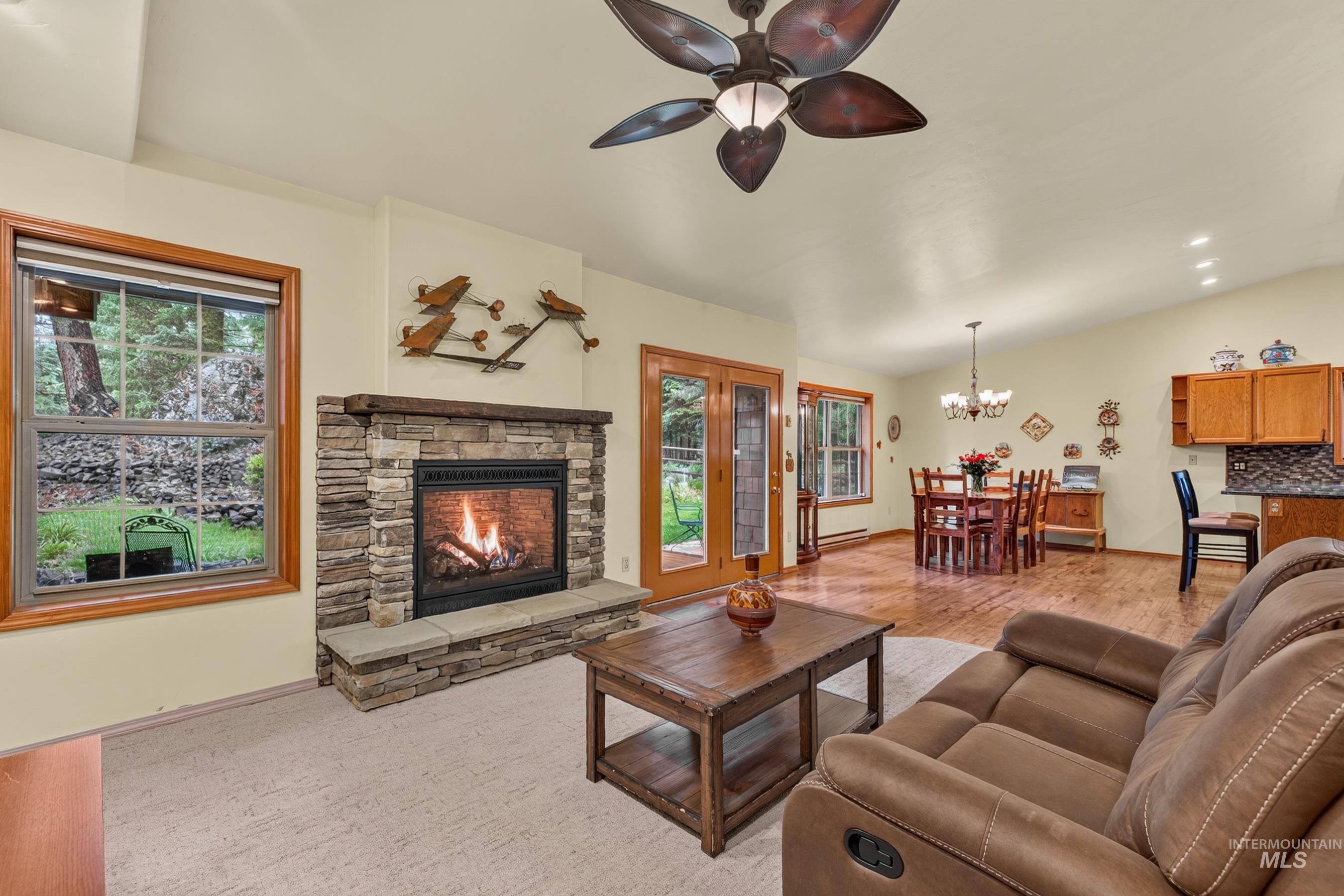 Living area featuring a stone-clad fireplace with hearth, wood-frame windows, and a ceiling fan