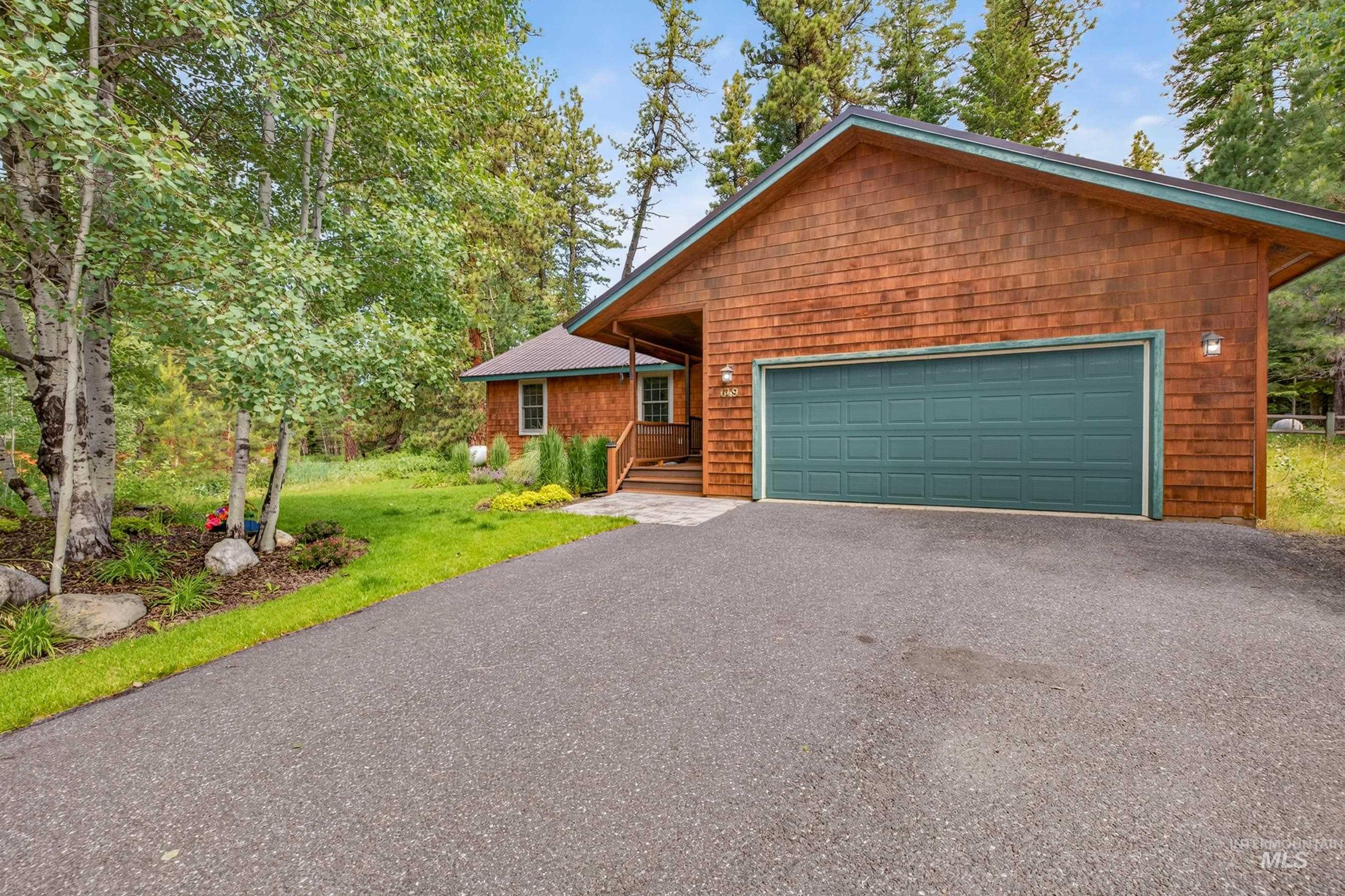 Wood-shingle exterior with a prominent teal garage door, asphalt driveway, and stone paver walkway