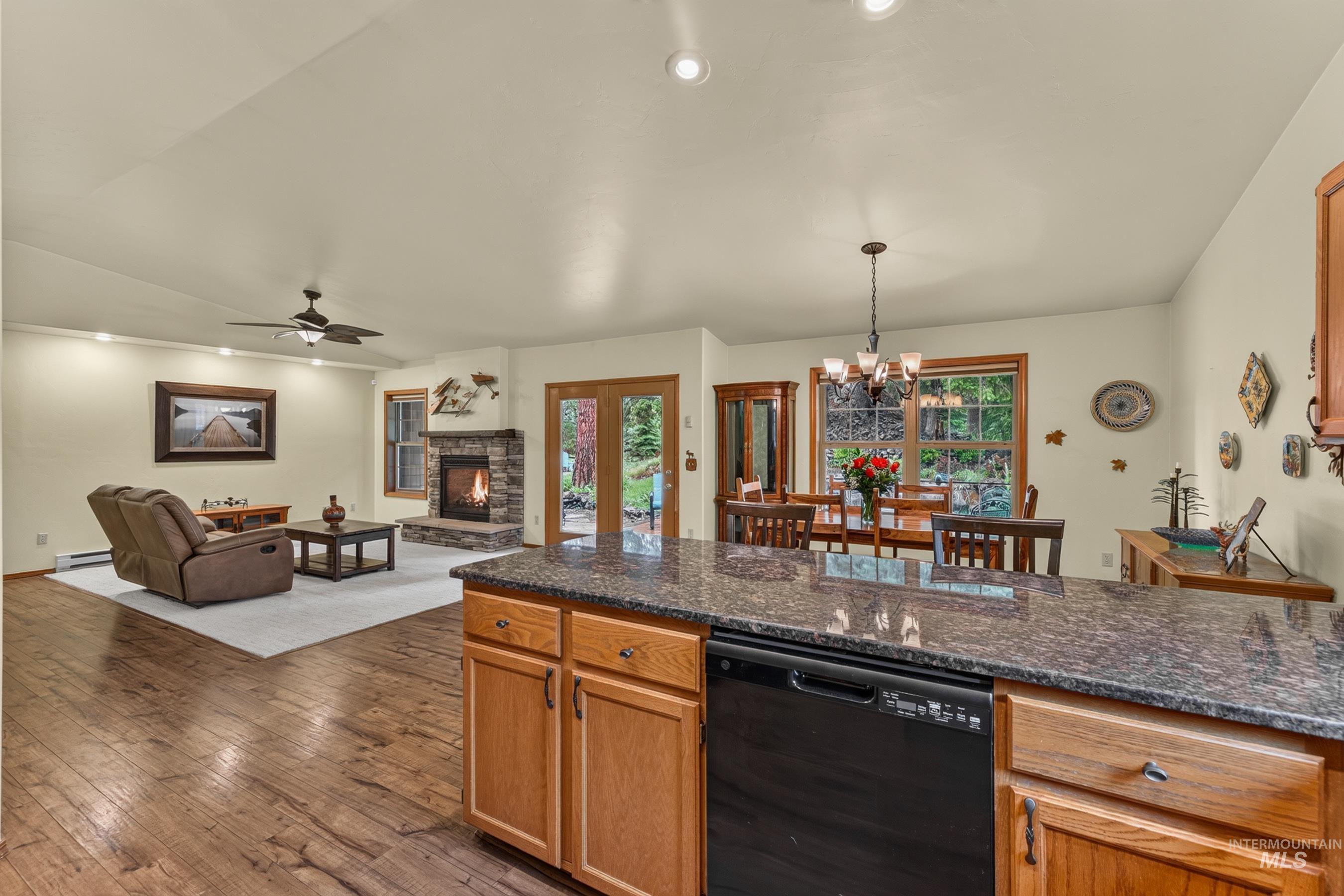 Open concept living area featuring wood-finish flooring, a stone-accented fireplace, and a dining area with outdoor access