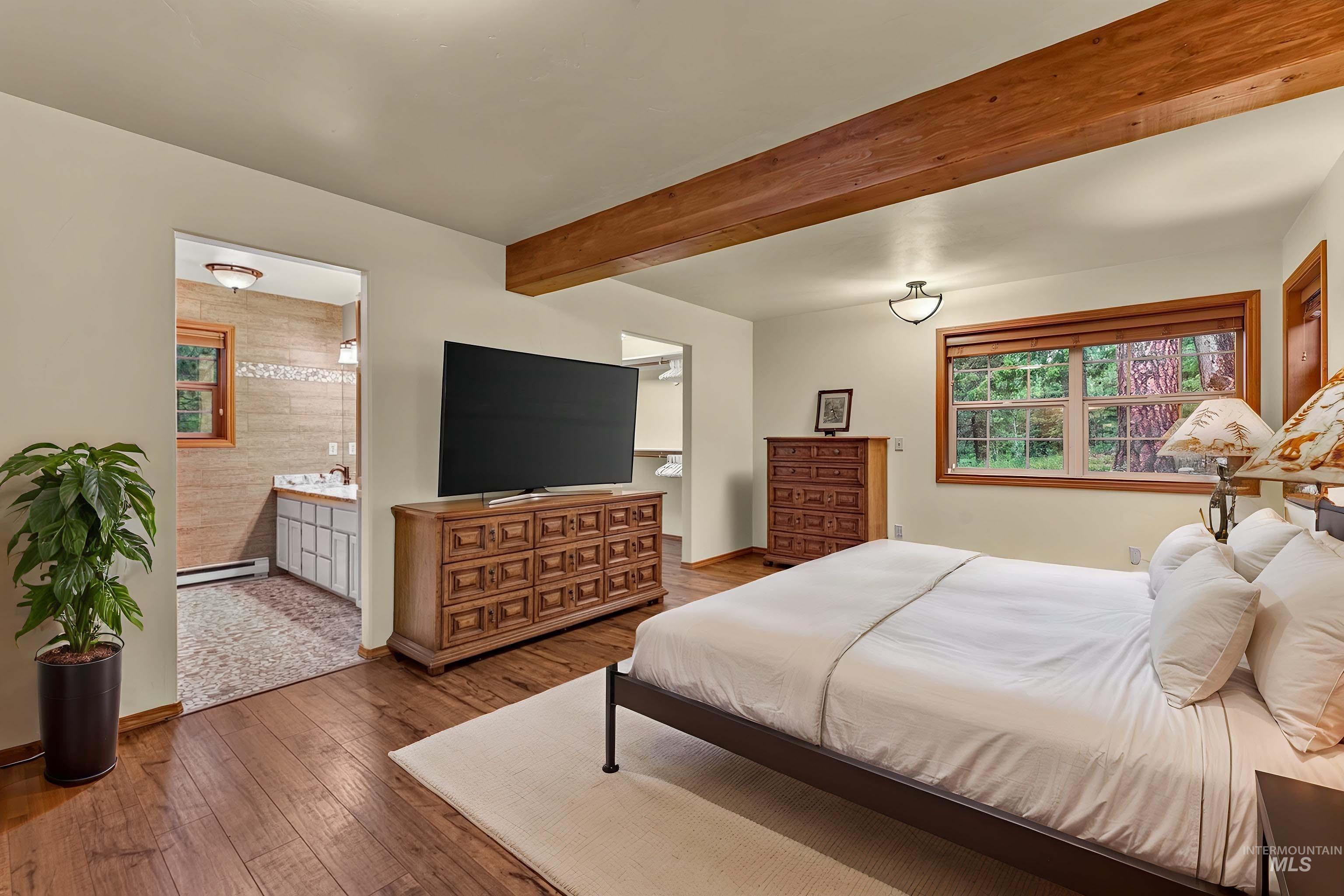 Spacious bedroom featuring wood-finish flooring, exposed wood ceiling beams, and a large window with wood trim