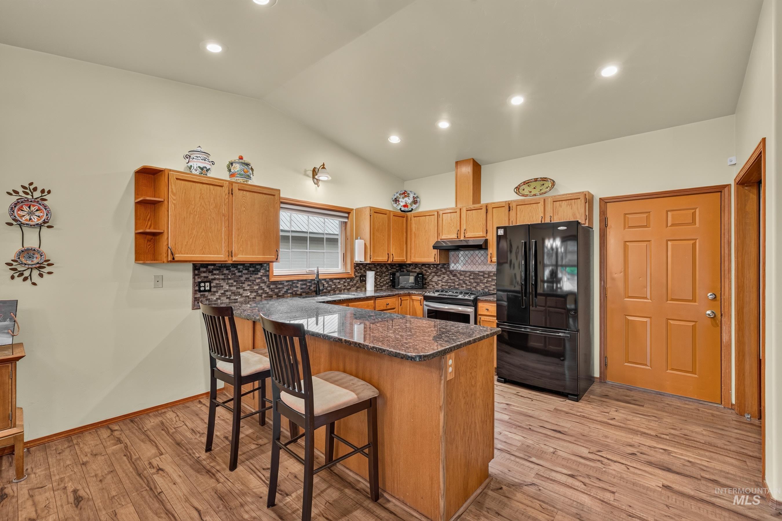 Kitchen featuring wood-finish flooring, a U-shaped countertop with a breakfast bar, wood cabinetry, a tile backsplash, and recessed lighting