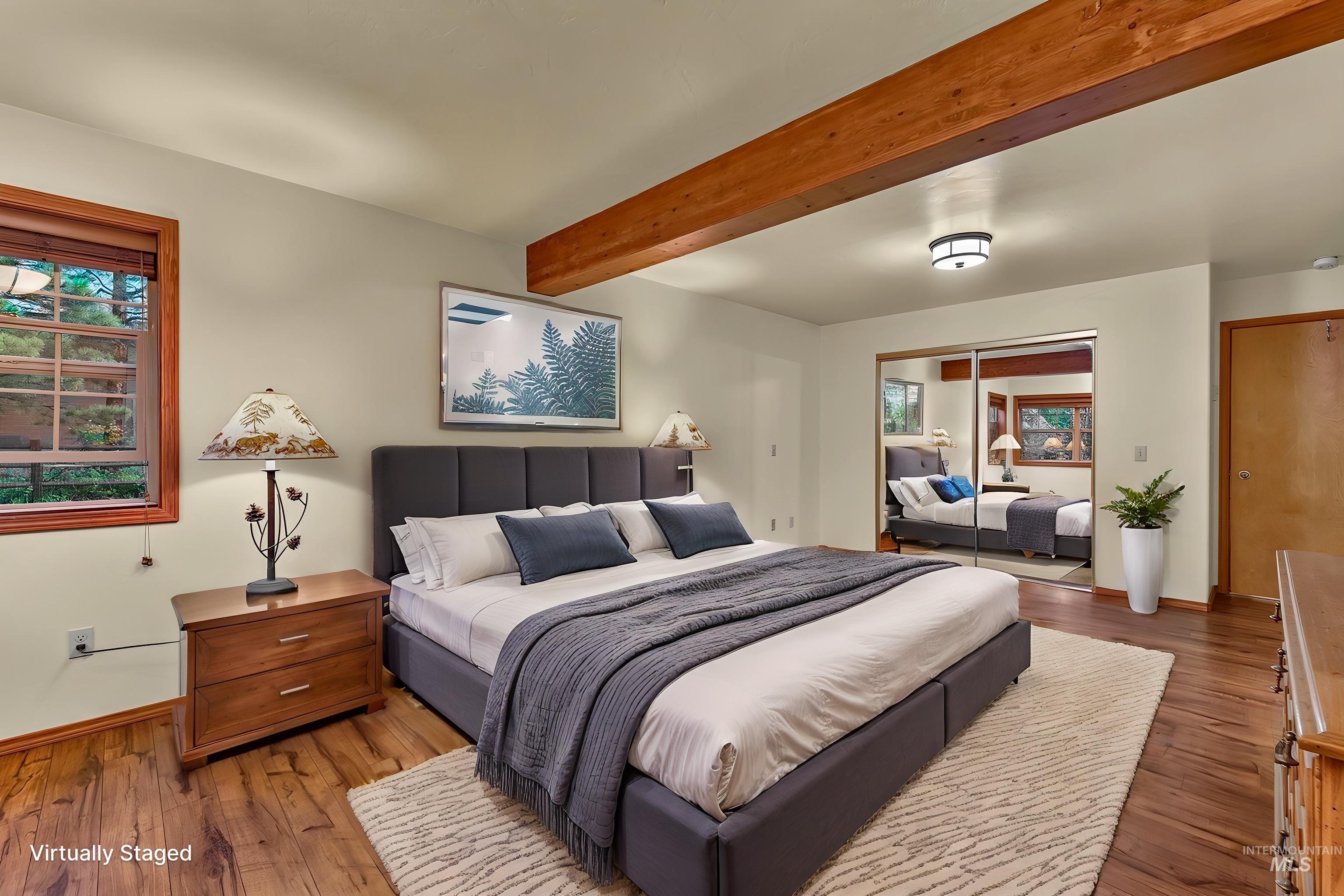Bedroom featuring exposed wood beams, wood-finish flooring, a window with wood trim, and mirrored closet doors