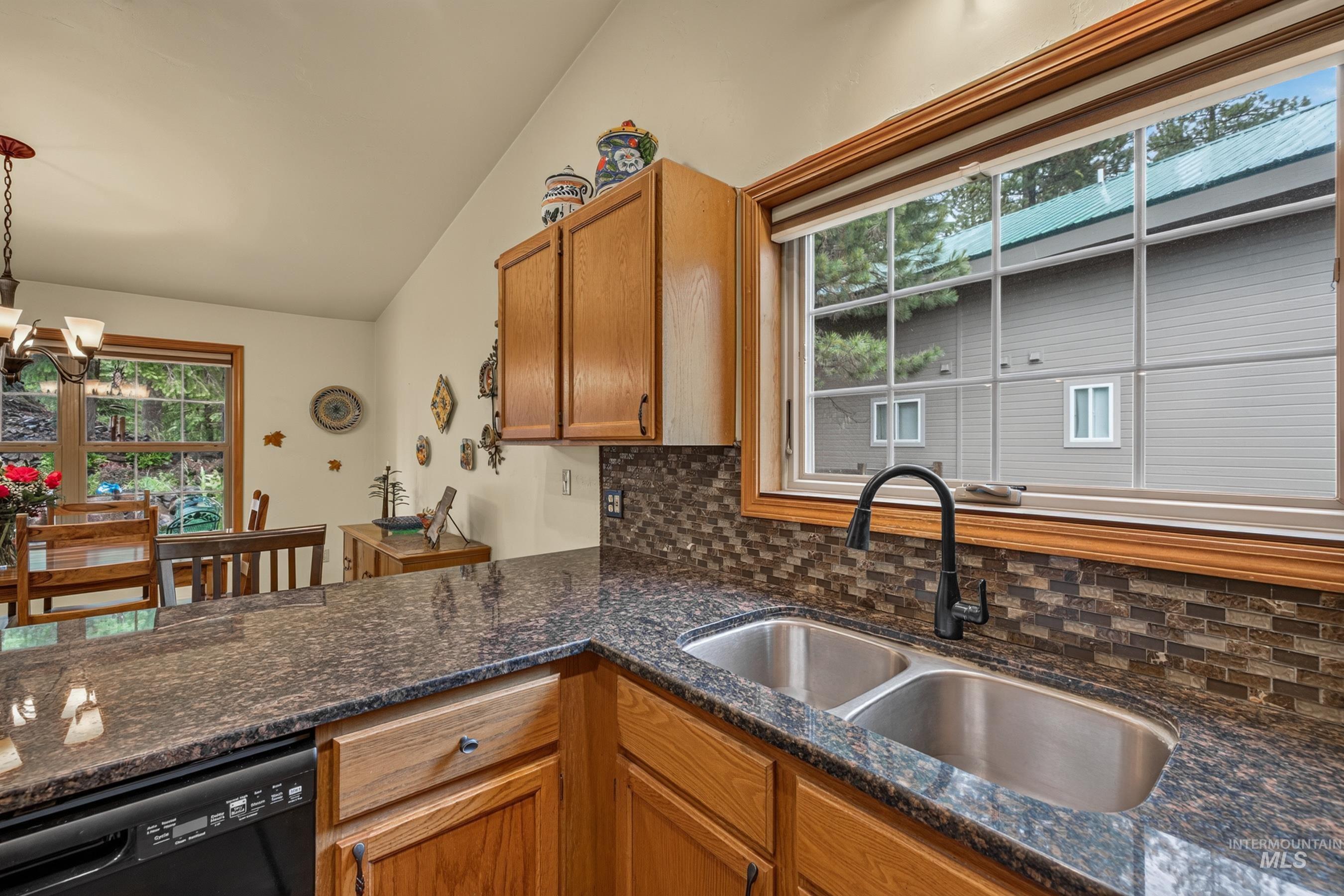 Kitchen featuring granite countertops, a double basin stainless steel sink with a matte black faucet, wood cabinetry, and a mosaic tile backsplash