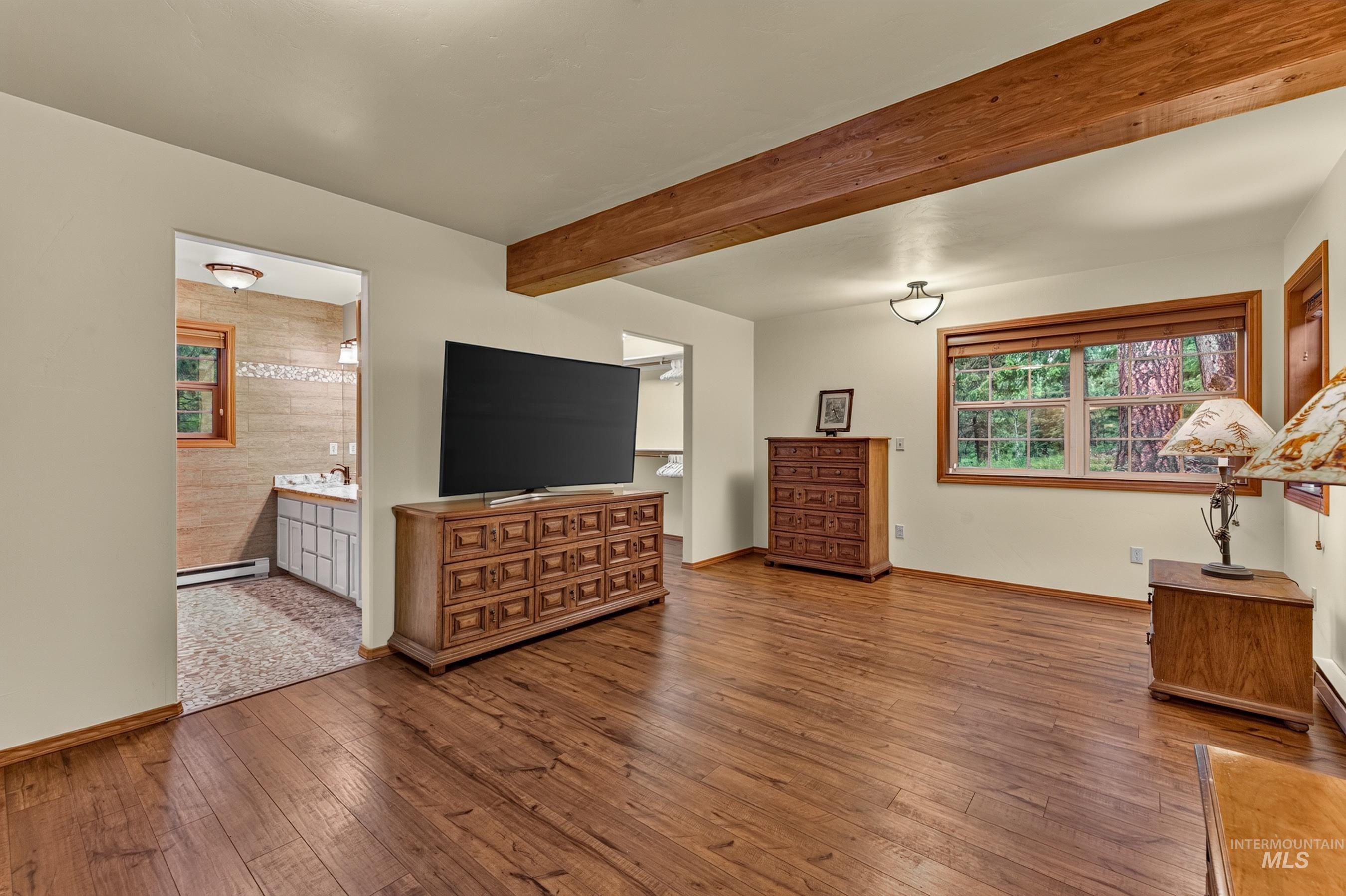 Spacious room featuring wood-finish flooring, a wood-trimmed window with exterior views, and a prominent wood ceiling beam