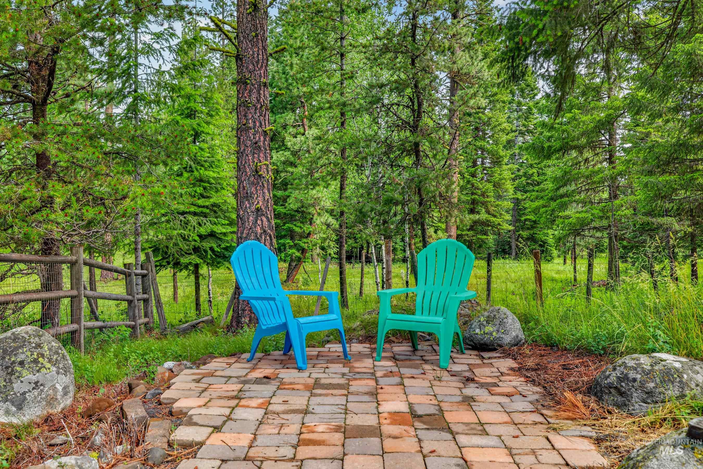 Paved brick patio surrounded by mature trees, natural rock elements, and a wooden split-rail fence