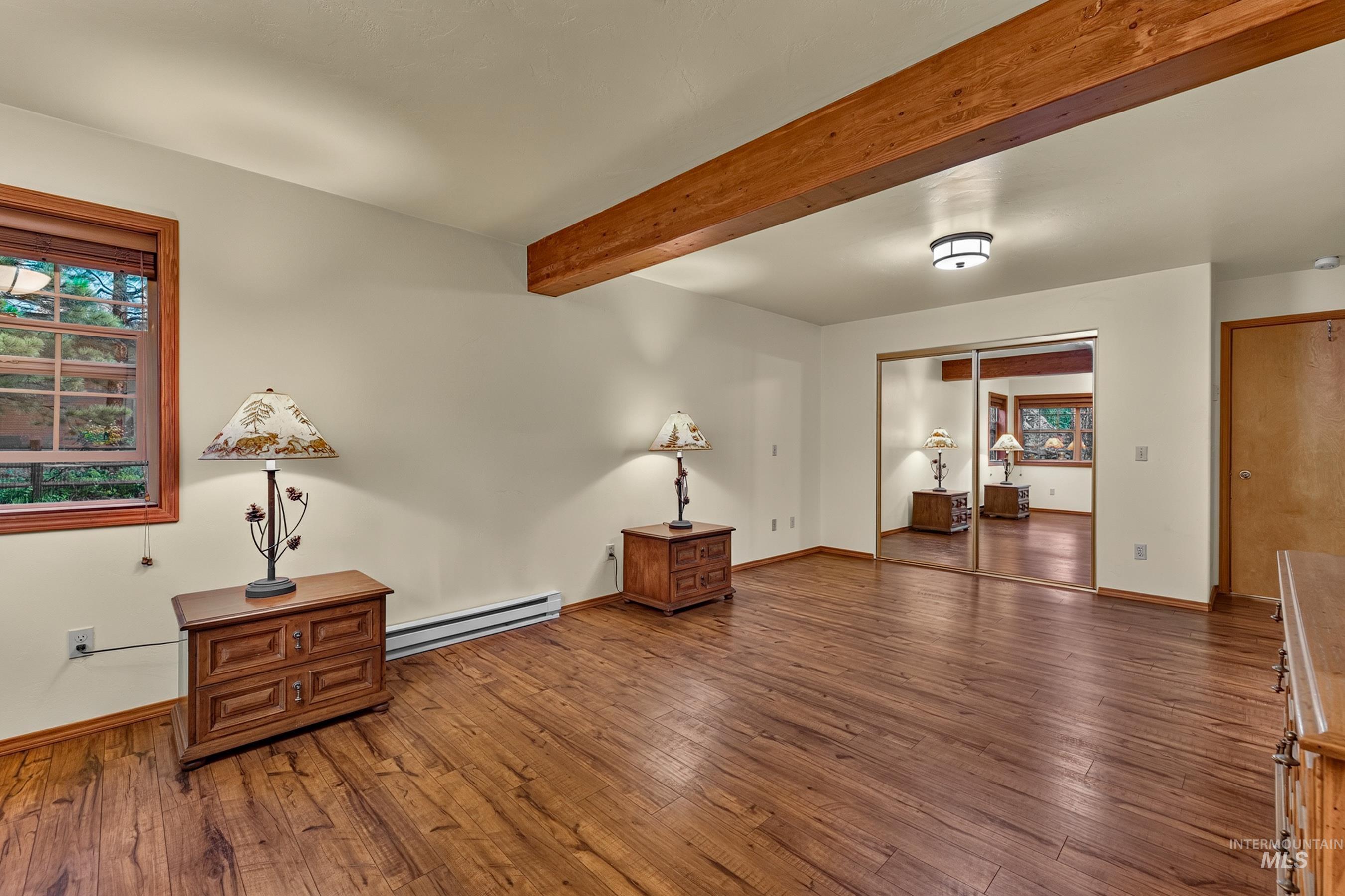 Spacious room featuring wood-finish flooring, a prominent exposed wood beam, mirrored closet doors, and wood-trimmed windows