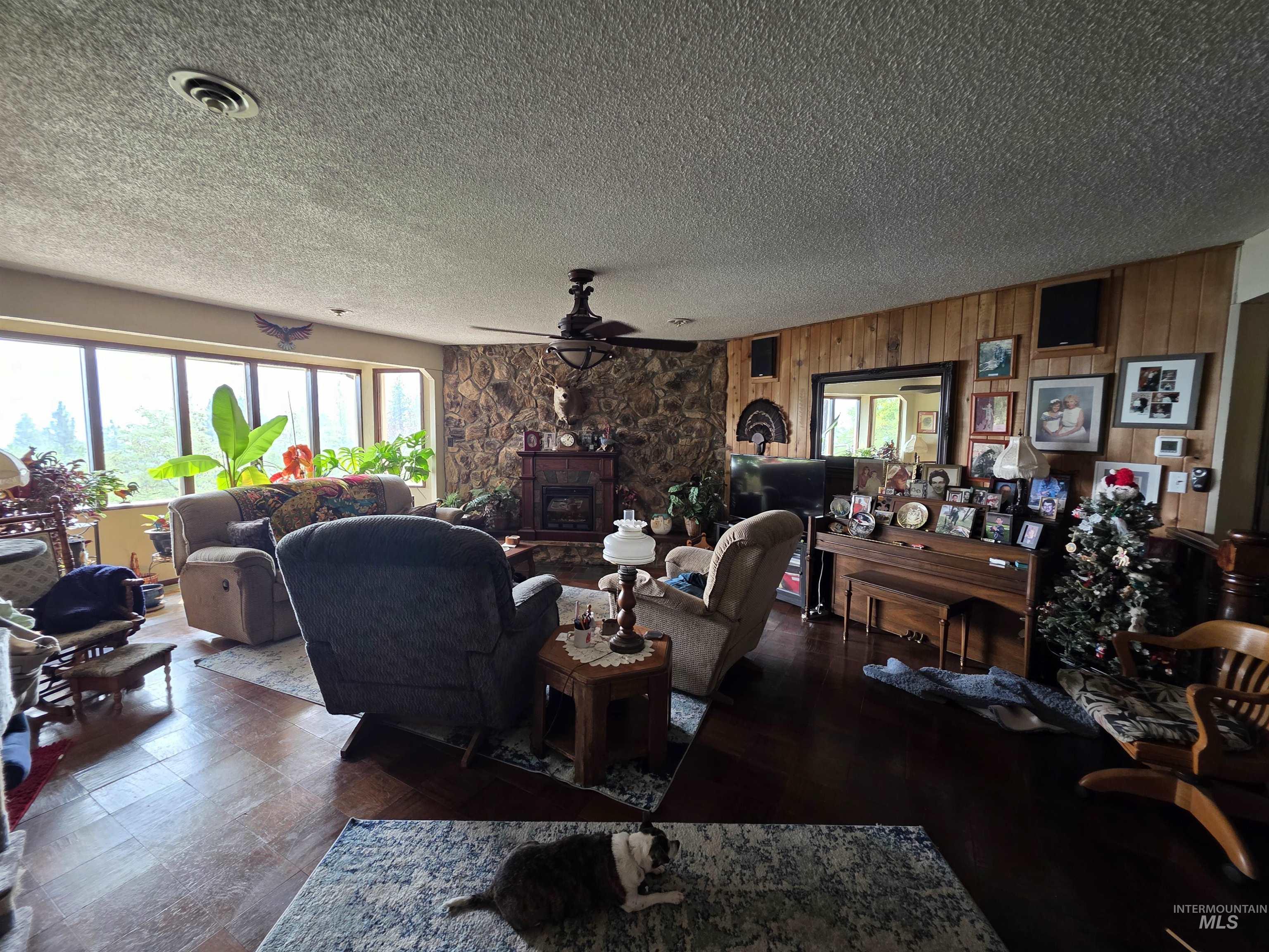Living room featuring a fireplace, ceiling fan, a textured ceiling, and wood walls