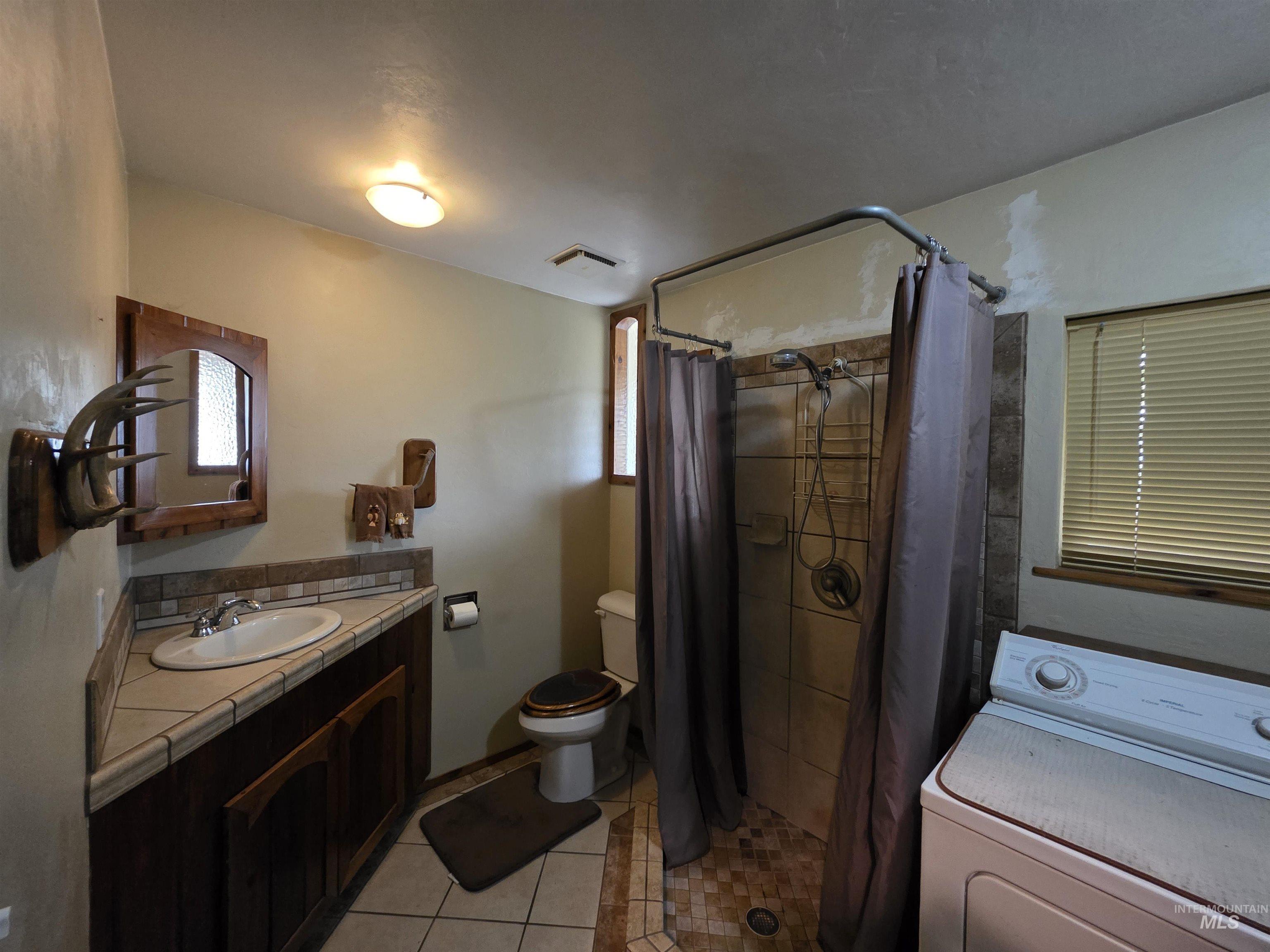 Bathroom with washer / clothes dryer, vanity, light tile patterned floors, and a stall shower