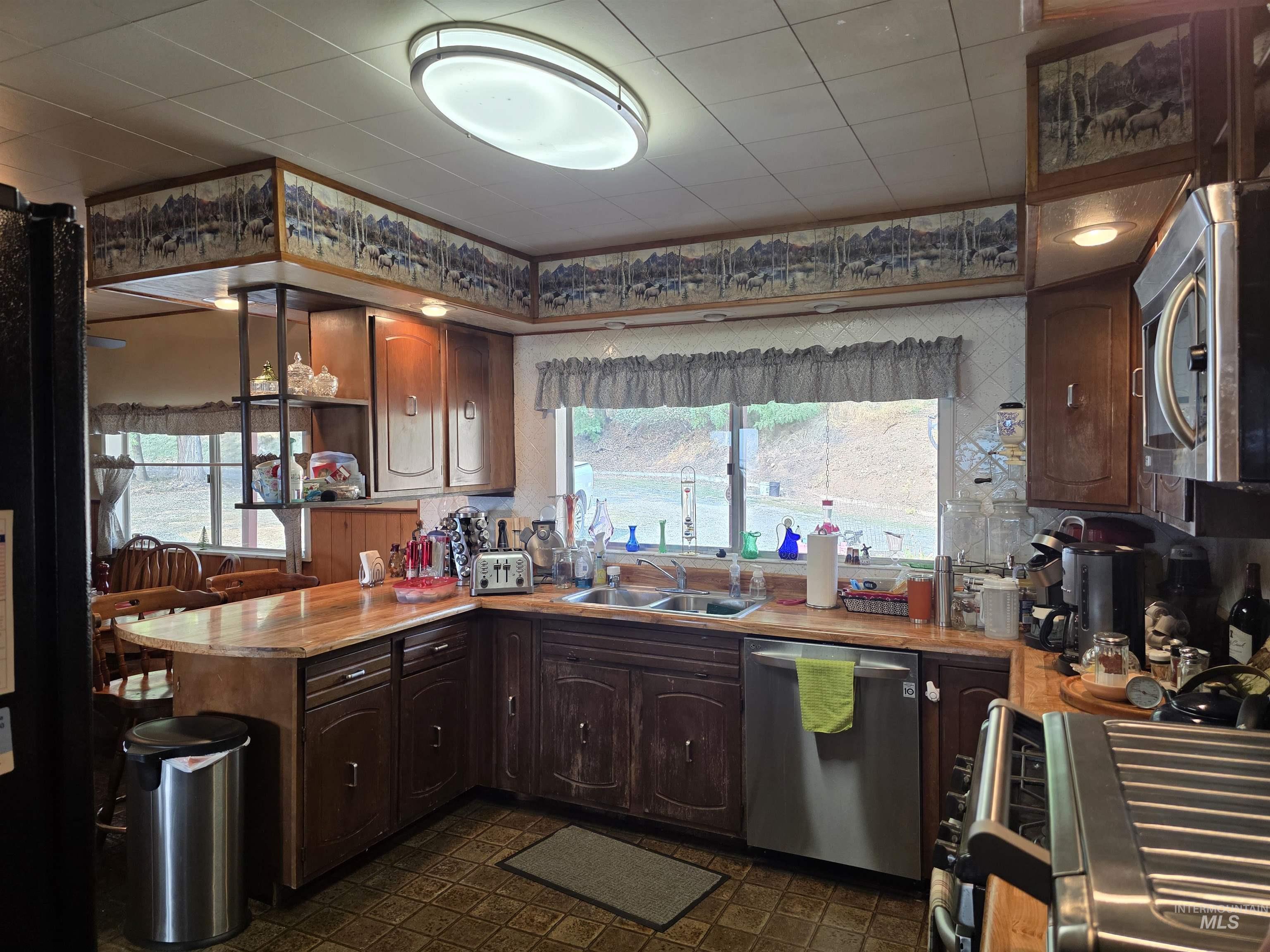Kitchen featuring a peninsula, appliances with stainless steel finishes, light countertops, and dark brown cabinets