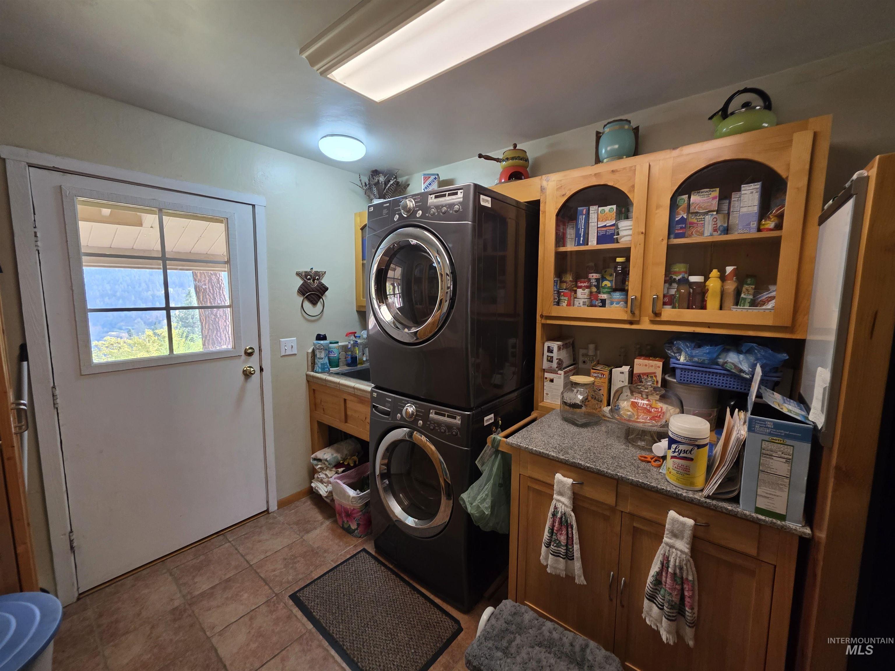 Laundry area featuring stacked washer and clothes dryer and light tile patterned floors