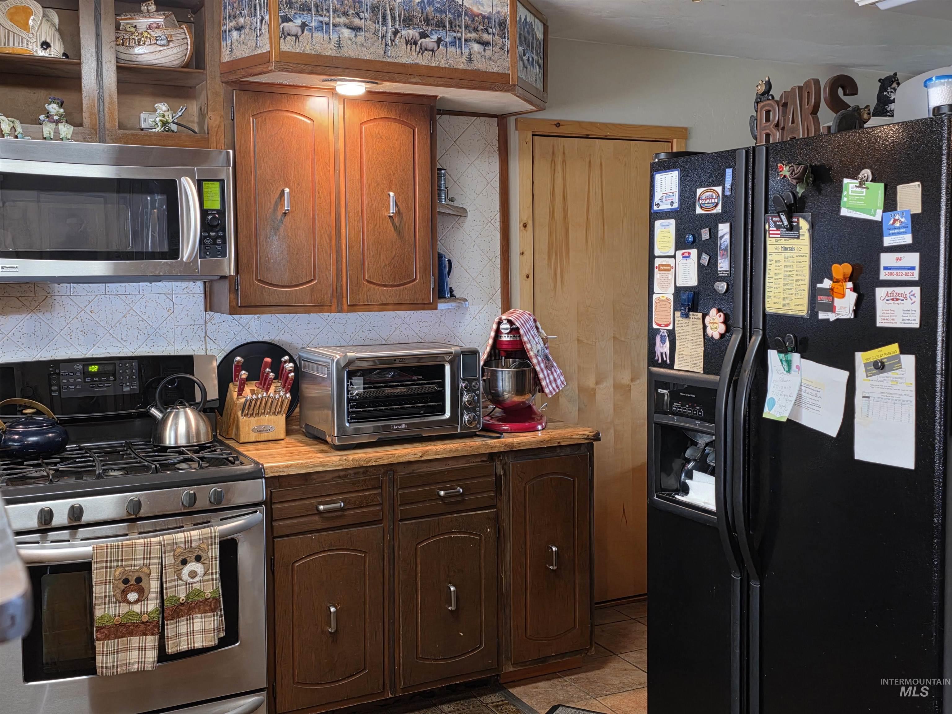 Kitchen with appliances with stainless steel finishes, decorative backsplash, light countertops, brown cabinetry, and light tile patterned floors