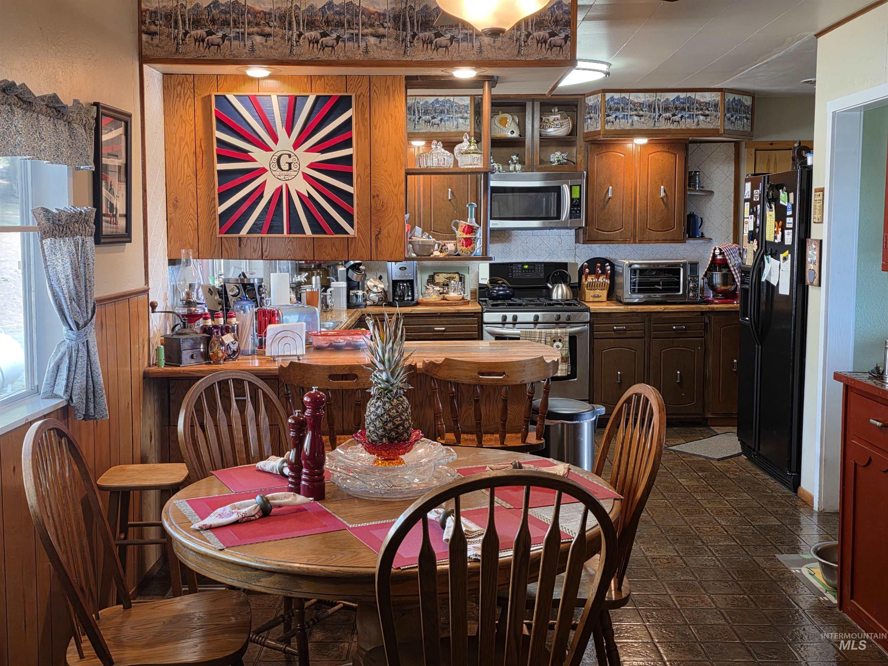 Kitchen with brown cabinetry, stainless steel appliances, wooden walls, and open shelves