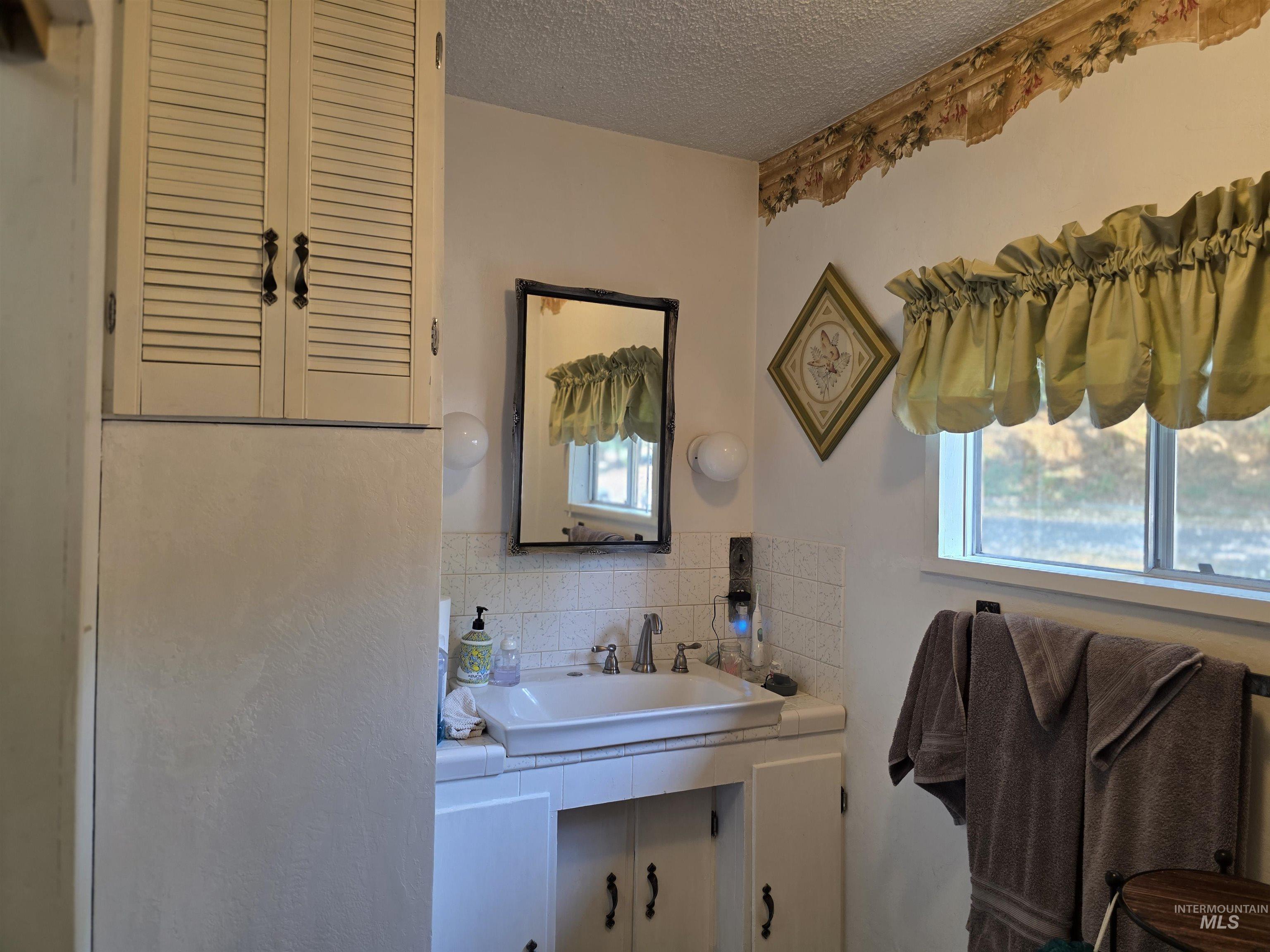 Bathroom with a textured ceiling, tasteful backsplash, and vanity