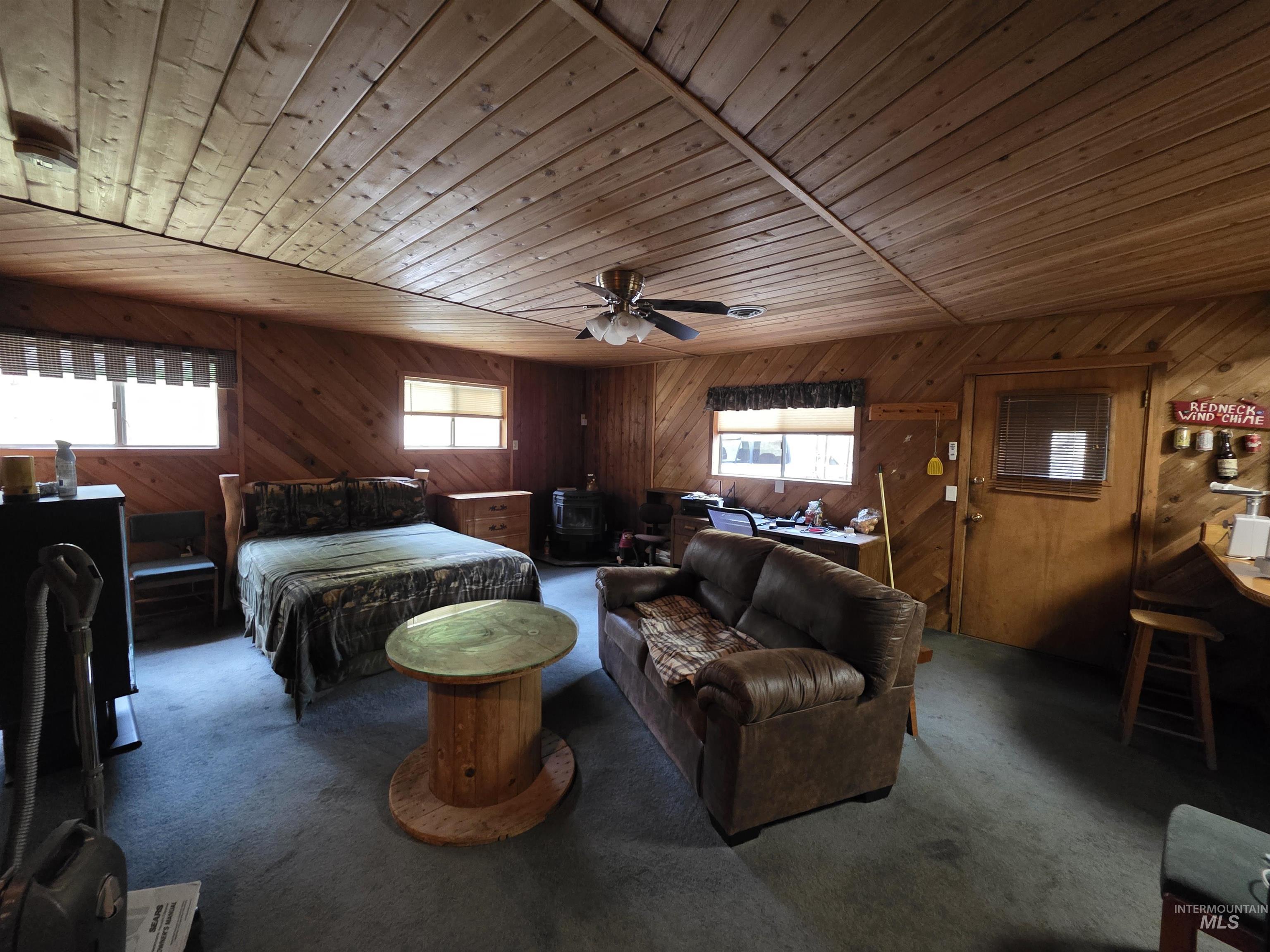 Bedroom featuring wood ceiling, wood walls, multiple windows, carpet flooring, and a wood stove