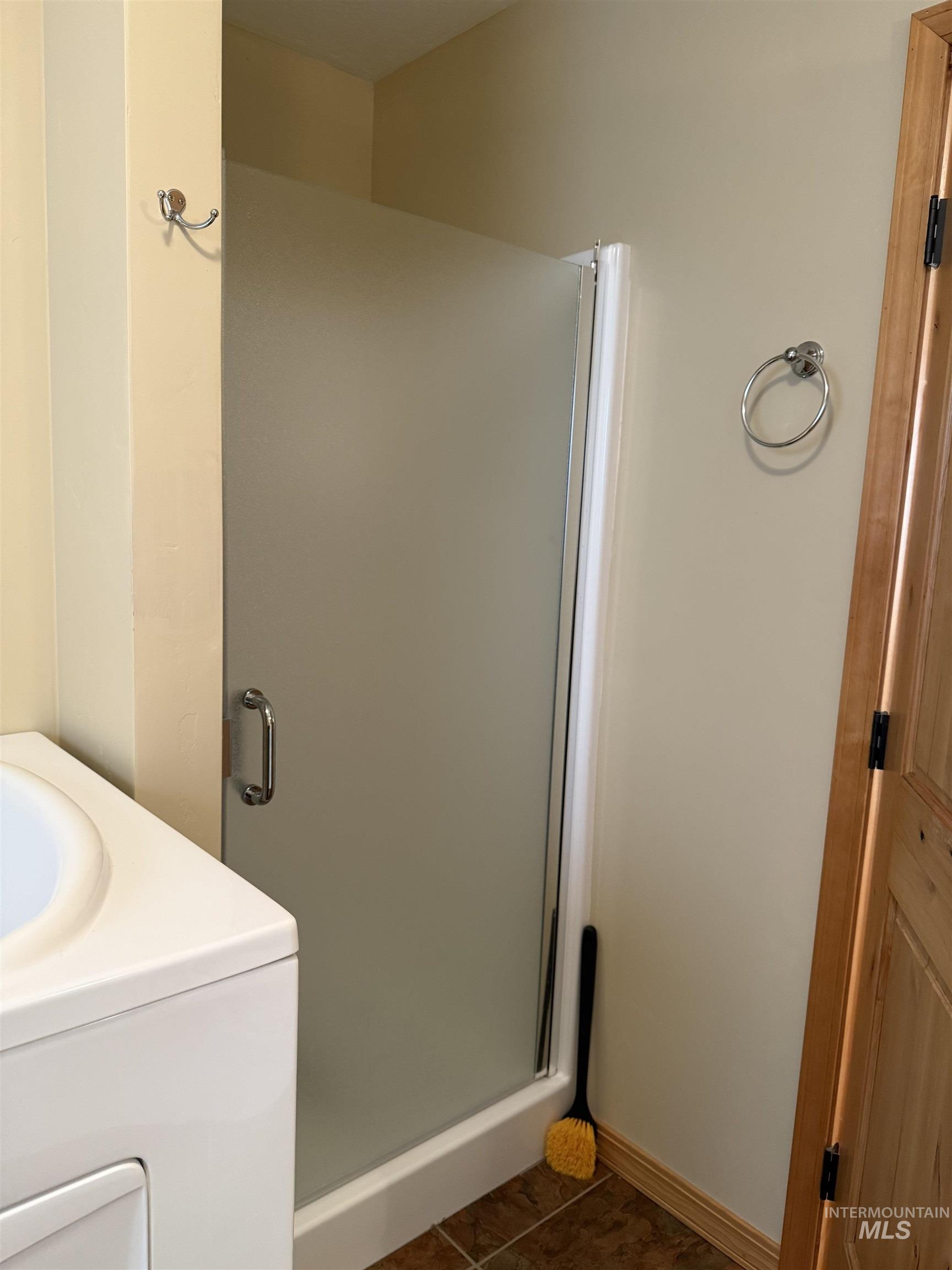 Full bath with vanity, a stall shower, washer / dryer, and dark tile patterned flooring