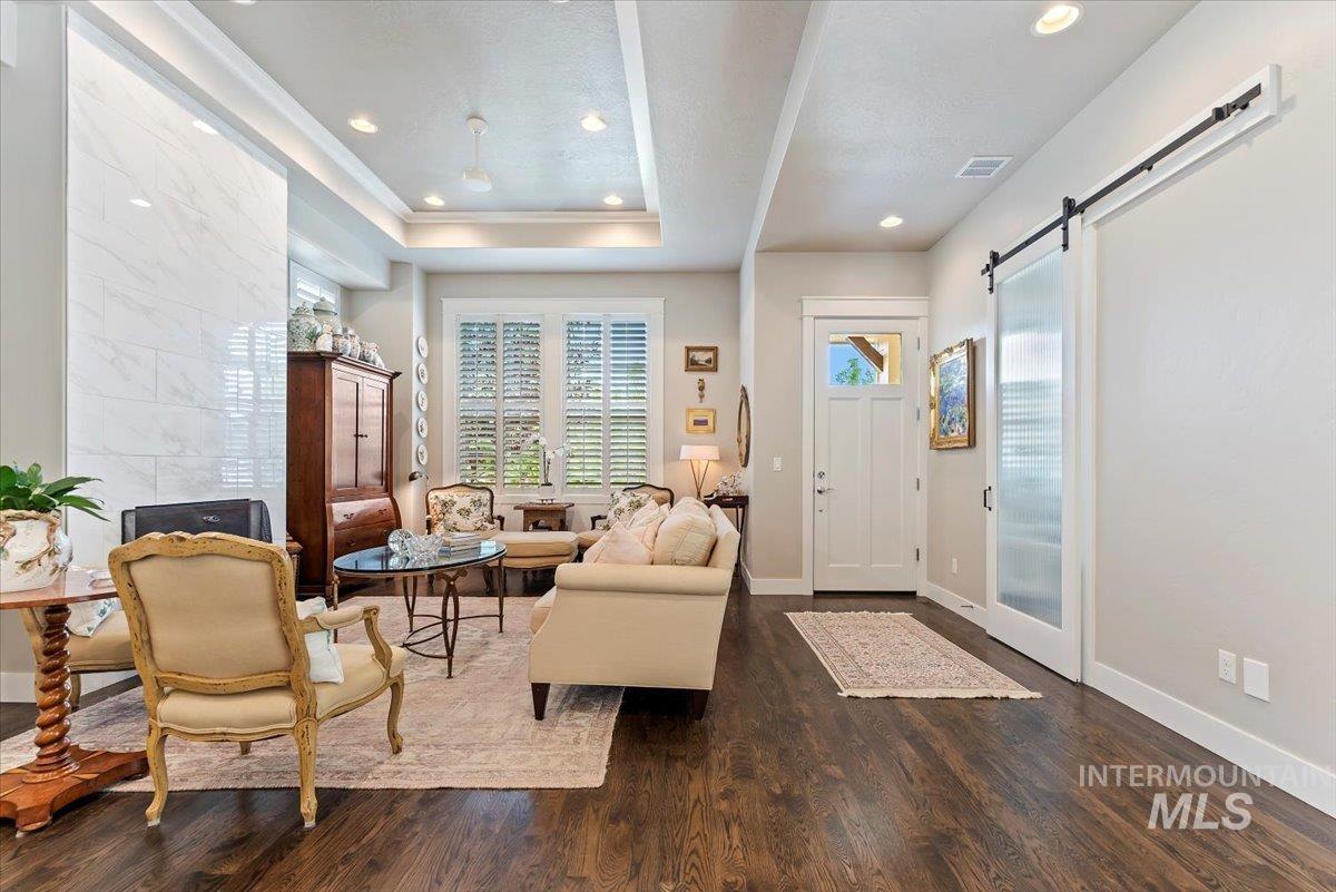 Living room featuring a barn door, healthy amount of natural light, dark wood-style floors, recessed lighting, and a tray ceiling