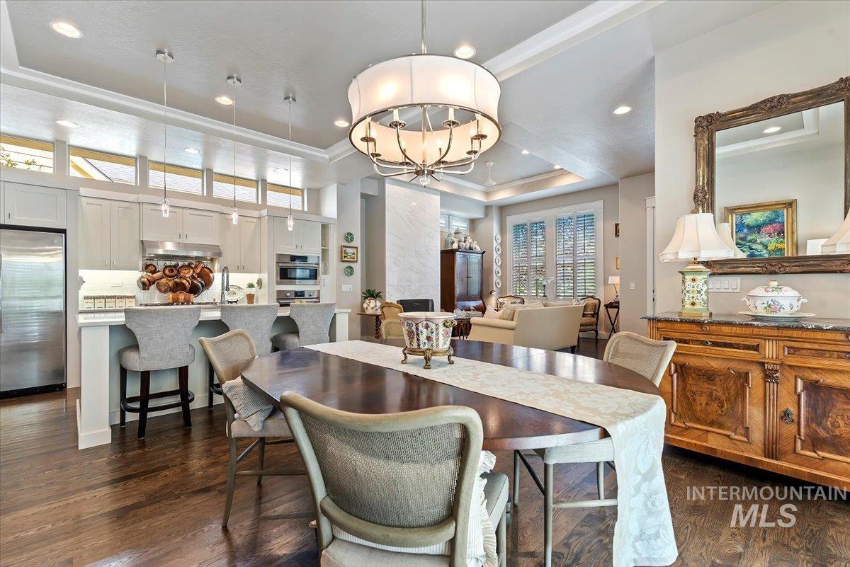 Dining space with a raised ceiling, a chandelier, dark wood-style floors, recessed lighting, and crown molding