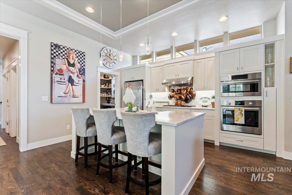 Kitchen featuring a breakfast bar, decorative light fixtures, recessed lighting, an island with sink, and dark wood finished floors