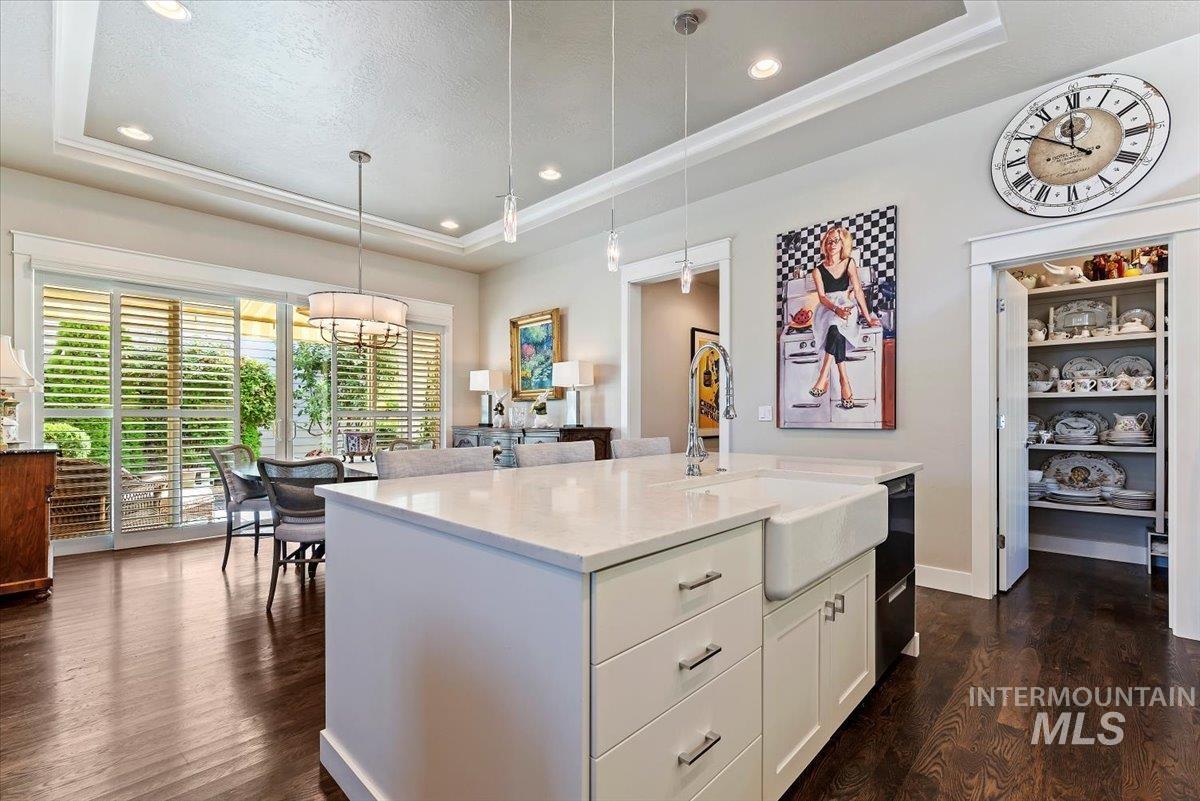 Kitchen featuring a tray ceiling, decorative light fixtures, white cabinetry, a kitchen island with sink, and dark wood-style flooring
