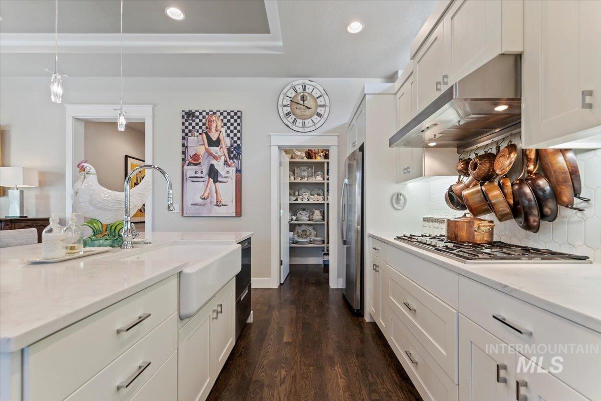 Kitchen featuring white cabinetry, decorative light fixtures, under cabinet range hood, dark wood-style flooring, and light stone countertops