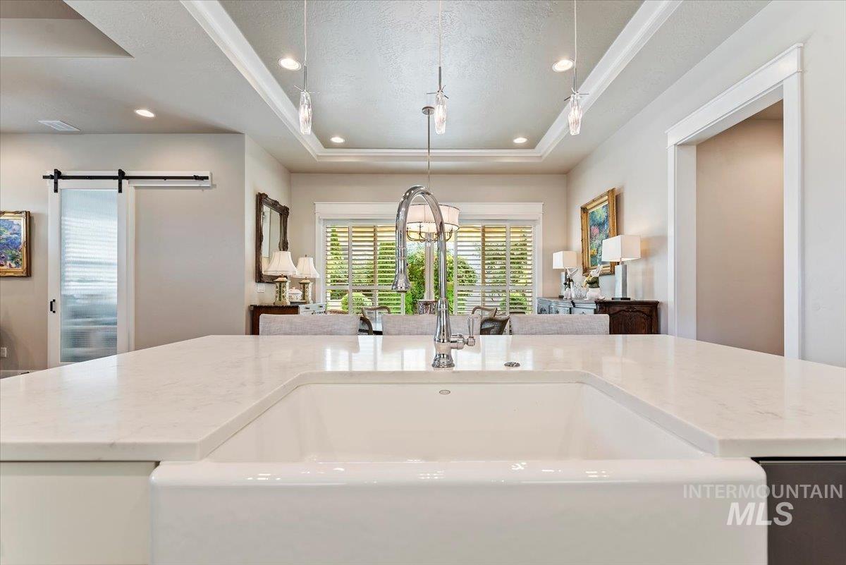 Kitchen with a raised ceiling, a barn door, light stone counters, a chandelier, and a textured ceiling