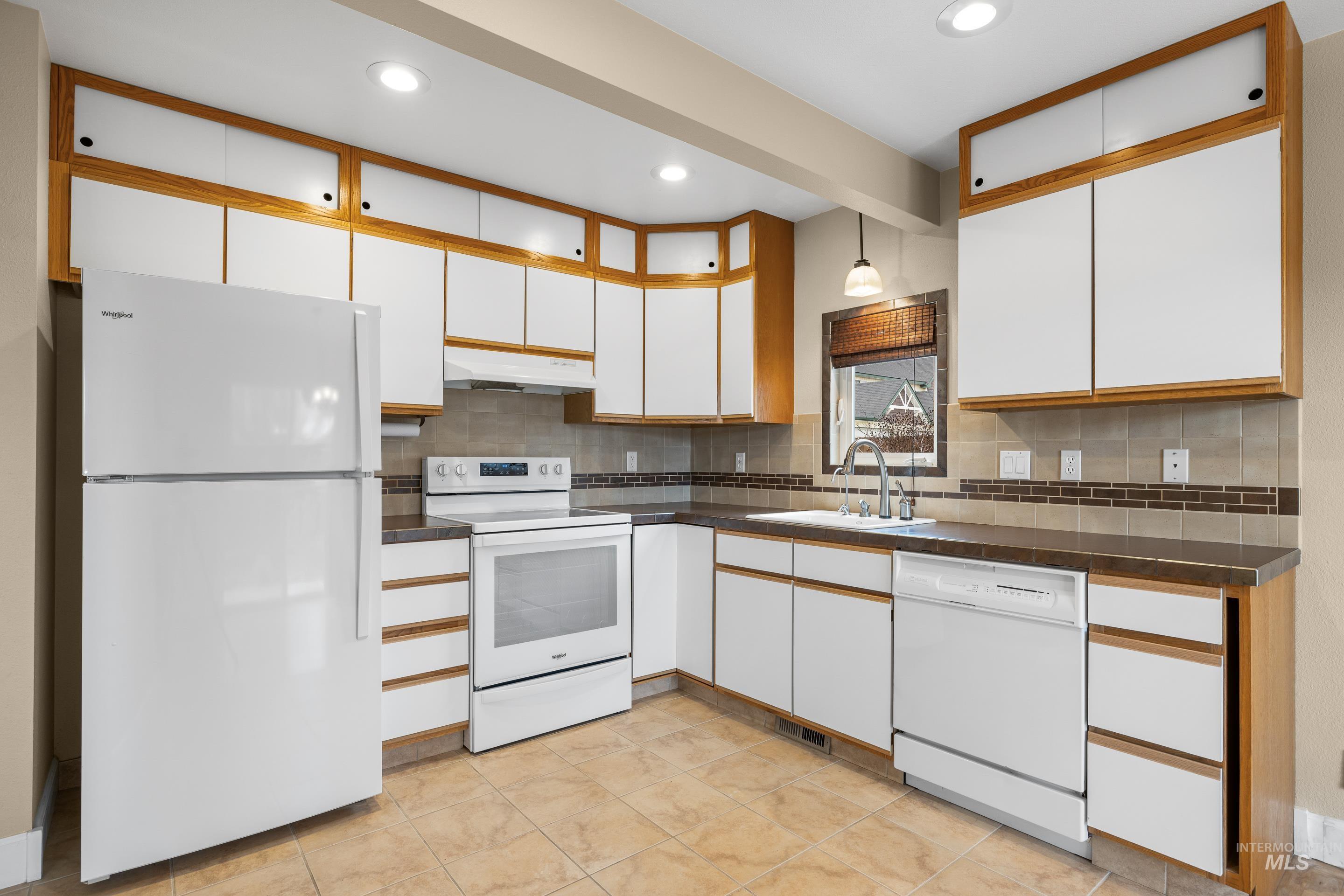 Two tone kitchen featuring two tone color scheme, white appliances, dark countertops, backsplash, and recessed lighting