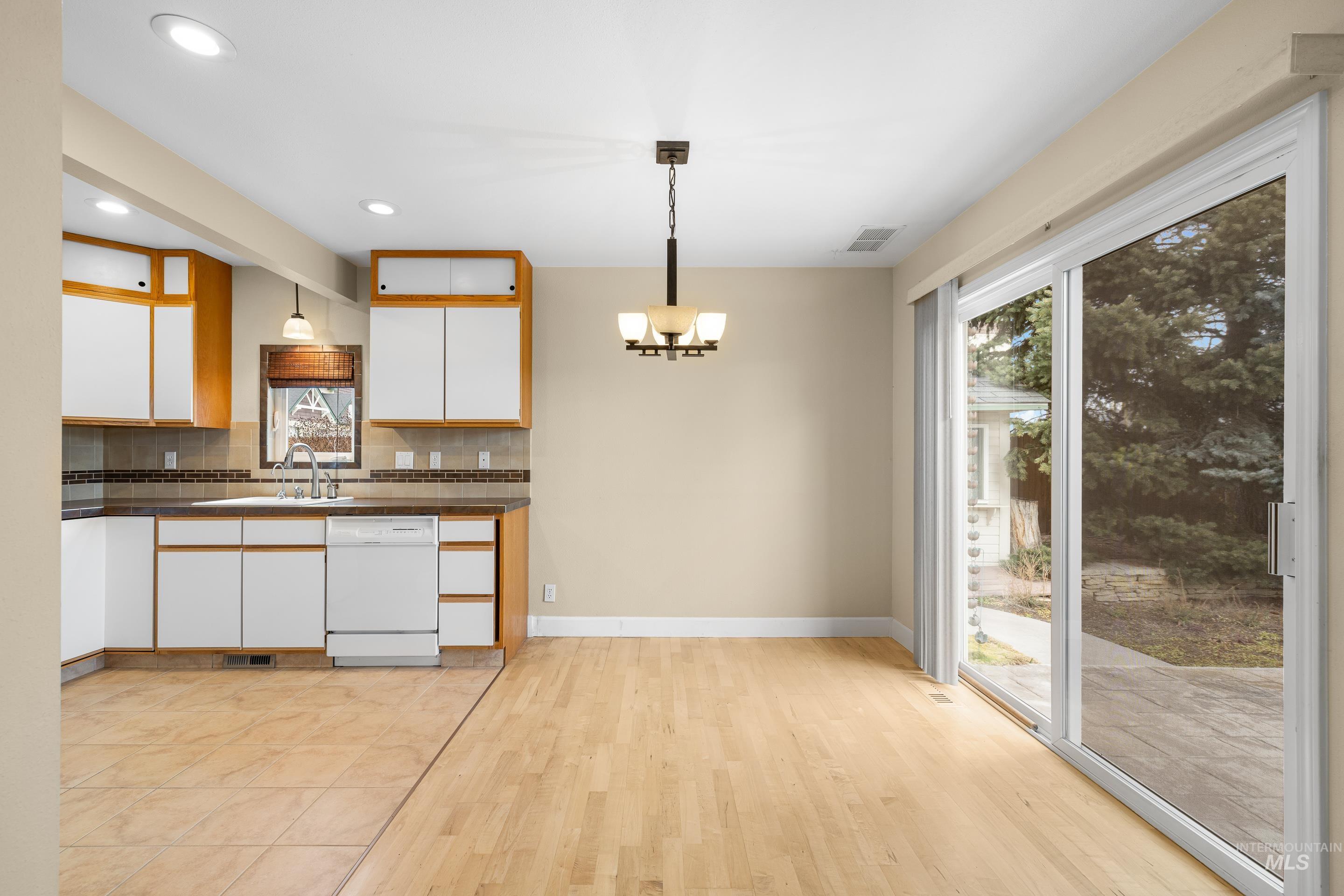 Kitchen featuring two tone cabinetry, dark countertops, white dishwasher, tasteful backsplash, and light wood finished floors