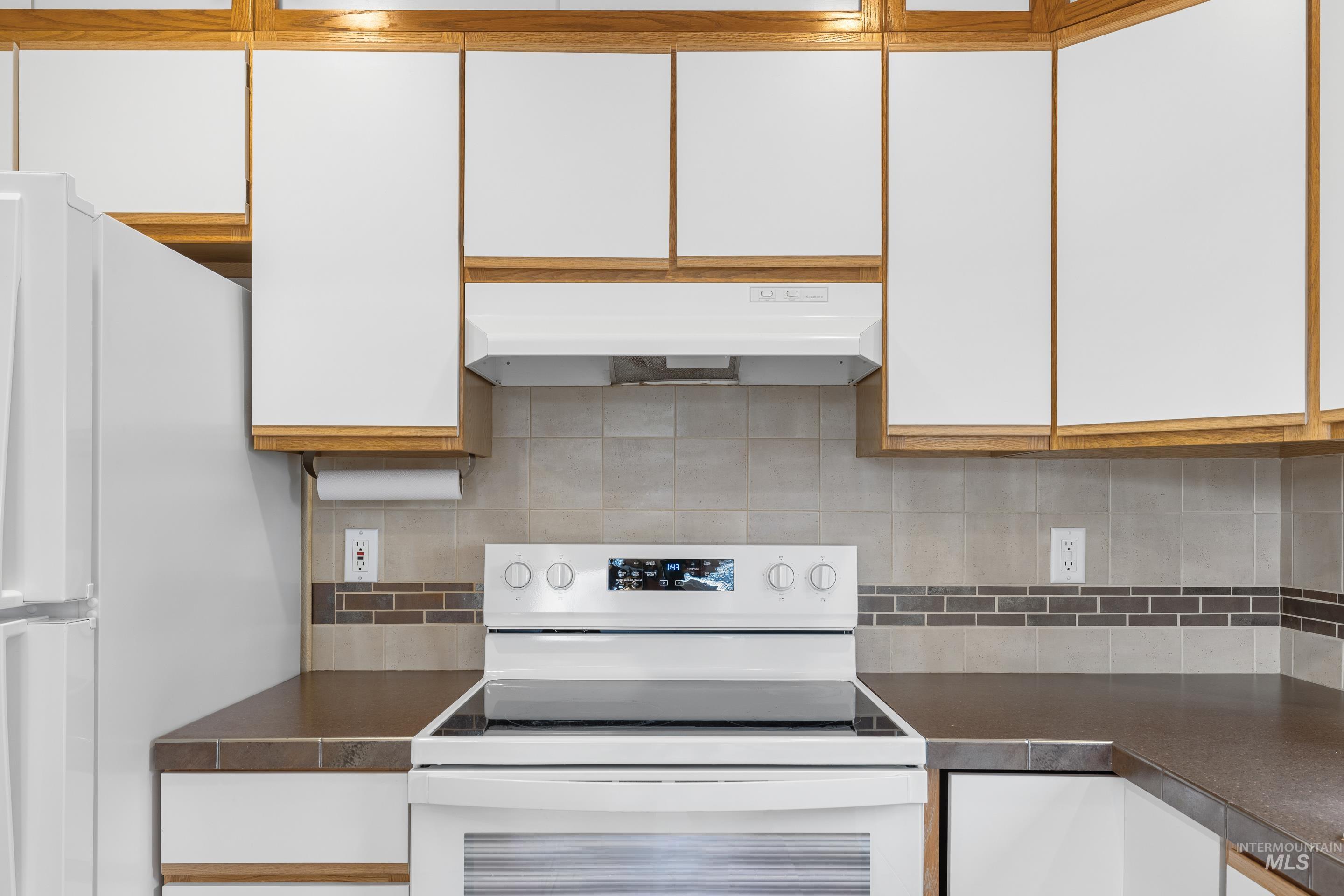 Kitchen with dark countertops, white appliances, tasteful backsplash, and dual tone cabinetry