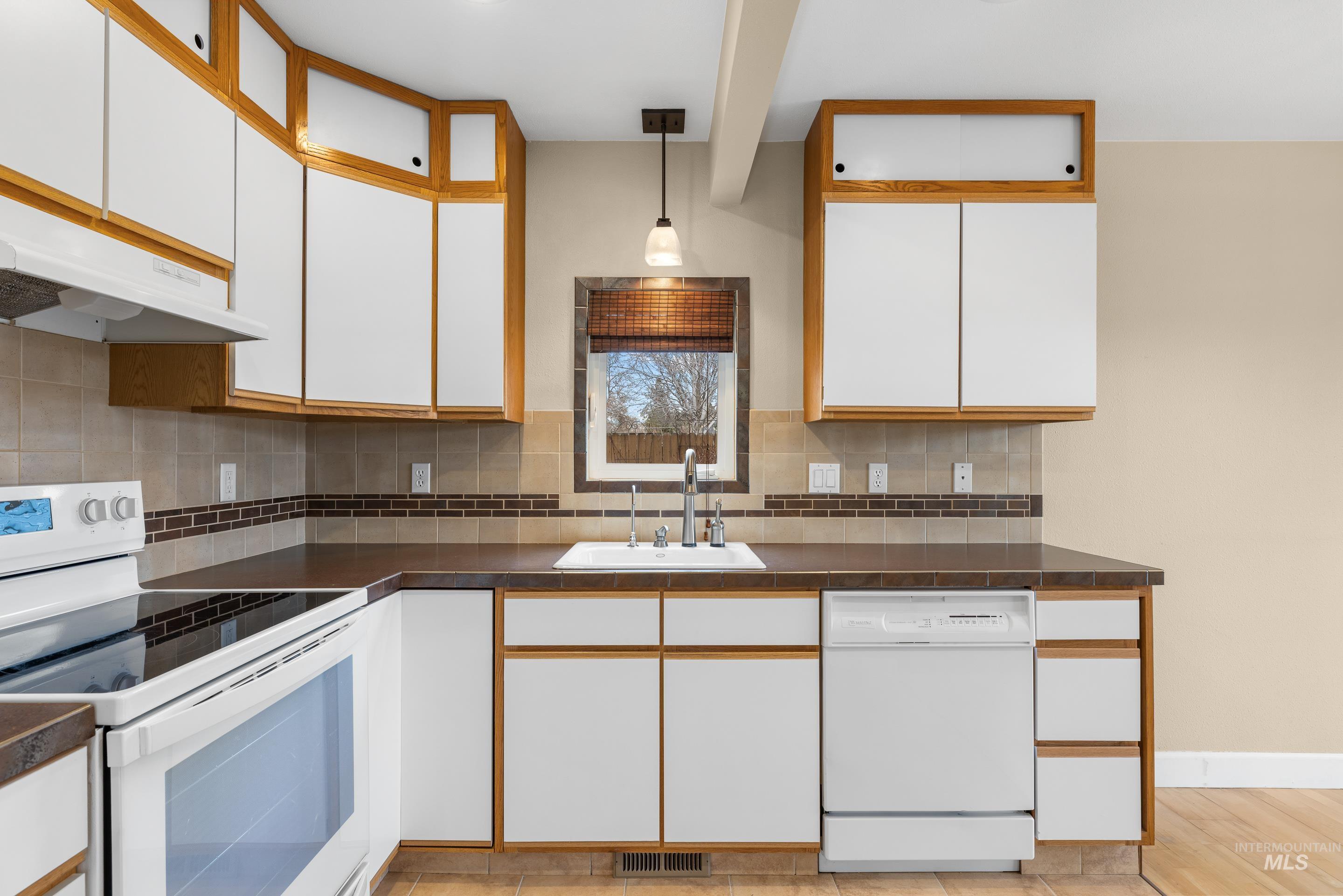 Dual tone kitchen featuring dual tone cabinetry, white appliances, dark countertops, decorative light fixtures, and tasteful backsplash