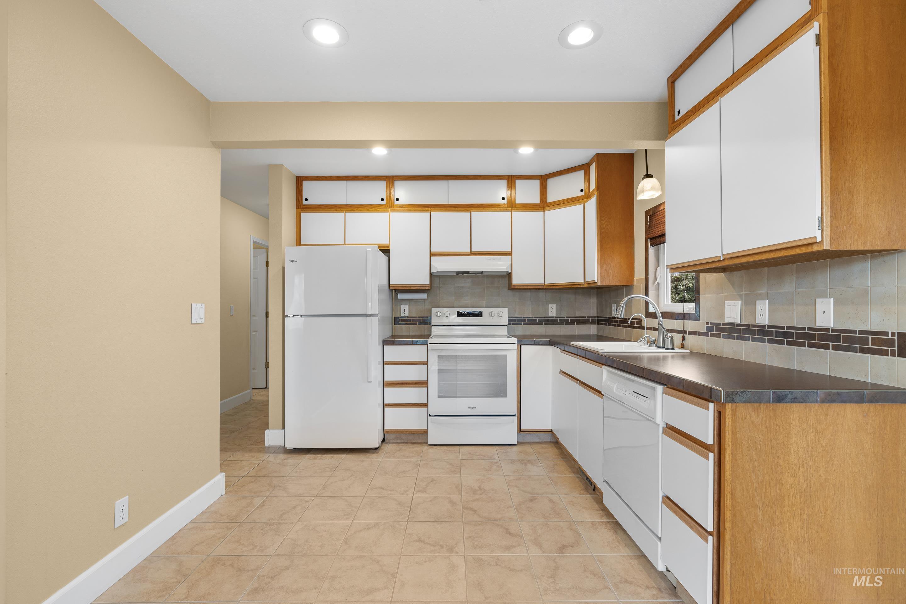 Kitchen with two tone color scheme, white appliances, backsplash, dark countertops, and recessed lighting