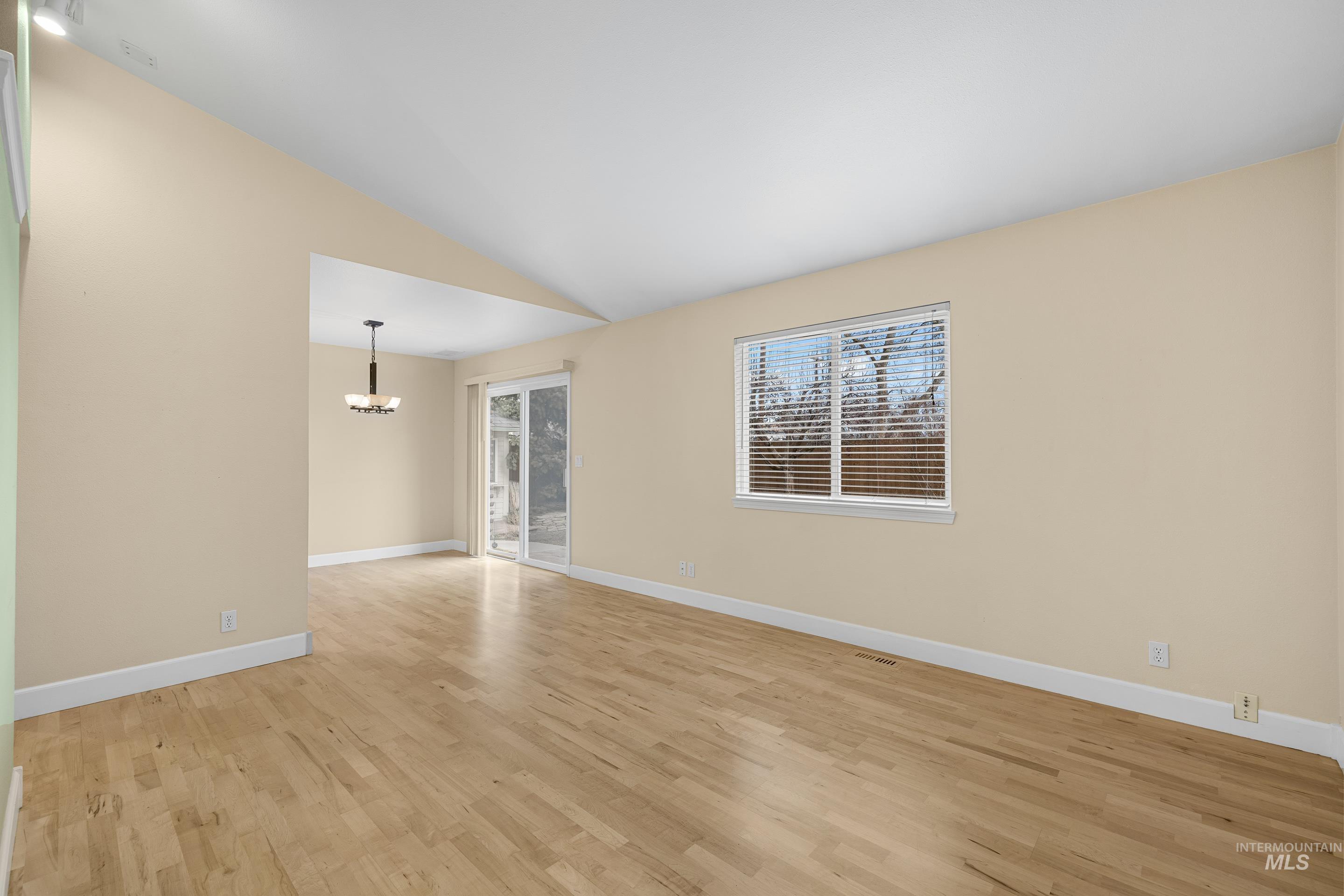Spare room featuring light wood-style flooring, vaulted ceiling, and suspended lighting