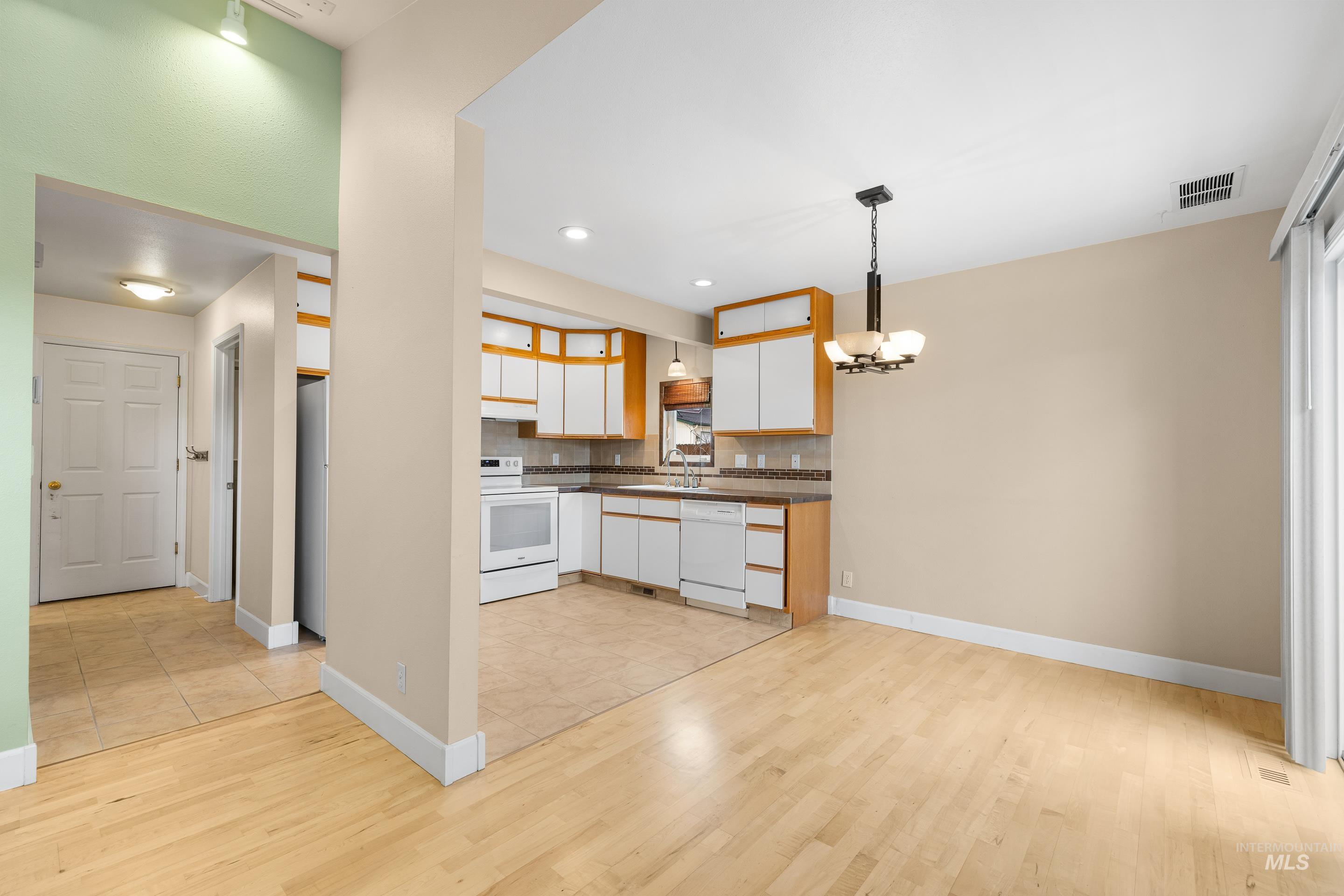 Kitchen featuring dual tone cabinets, dark countertops, white appliances, light wood-type flooring, and hanging lights